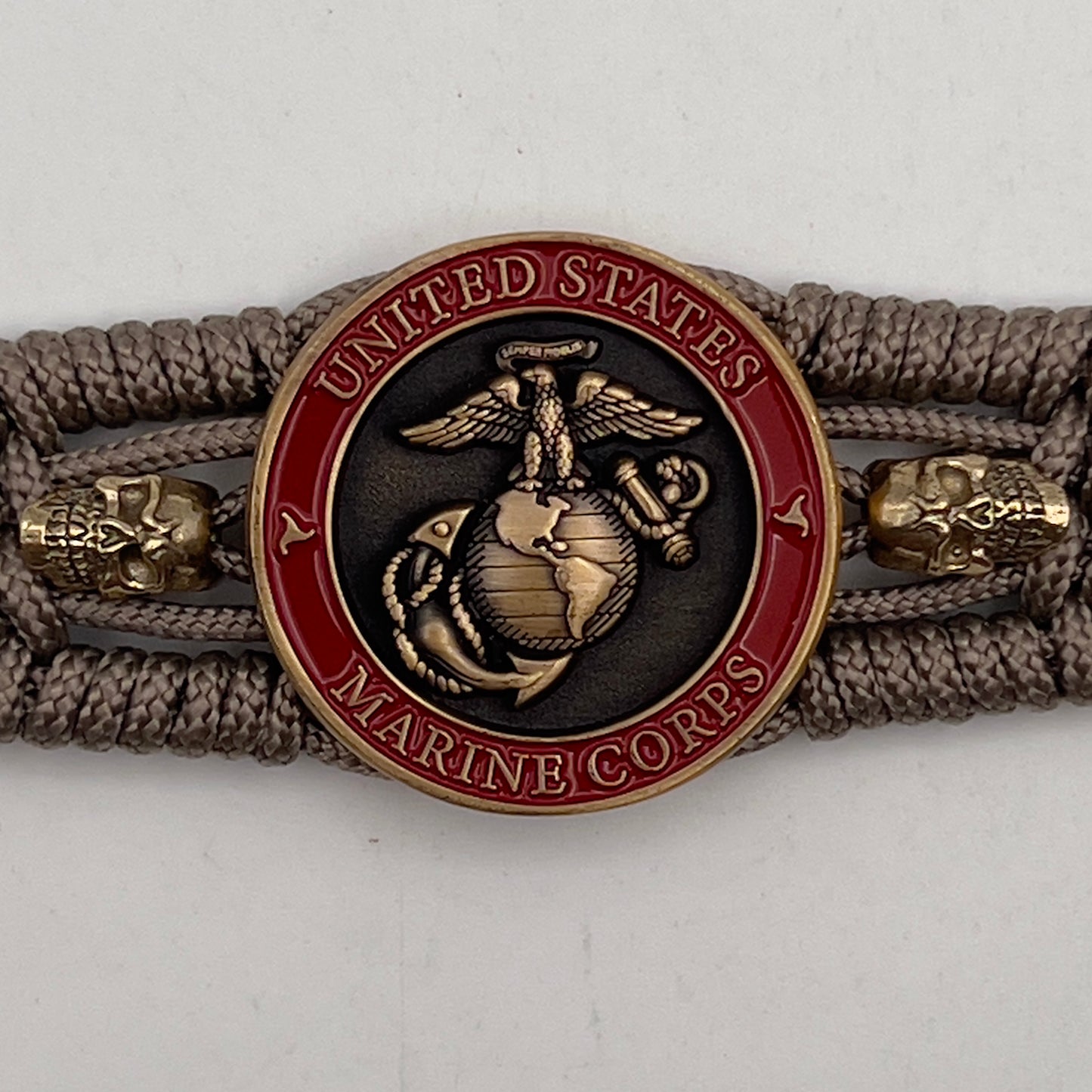 Thin, medium width, flexible and comfortable braided United States Marine Corps bracelet featuring a 24K antique gold plated USMC officer Eagle Globe and Anchor medallion, two gold plated skulls, a gold Cobra style tactical buckle and woven with tan Type-1 paracord.