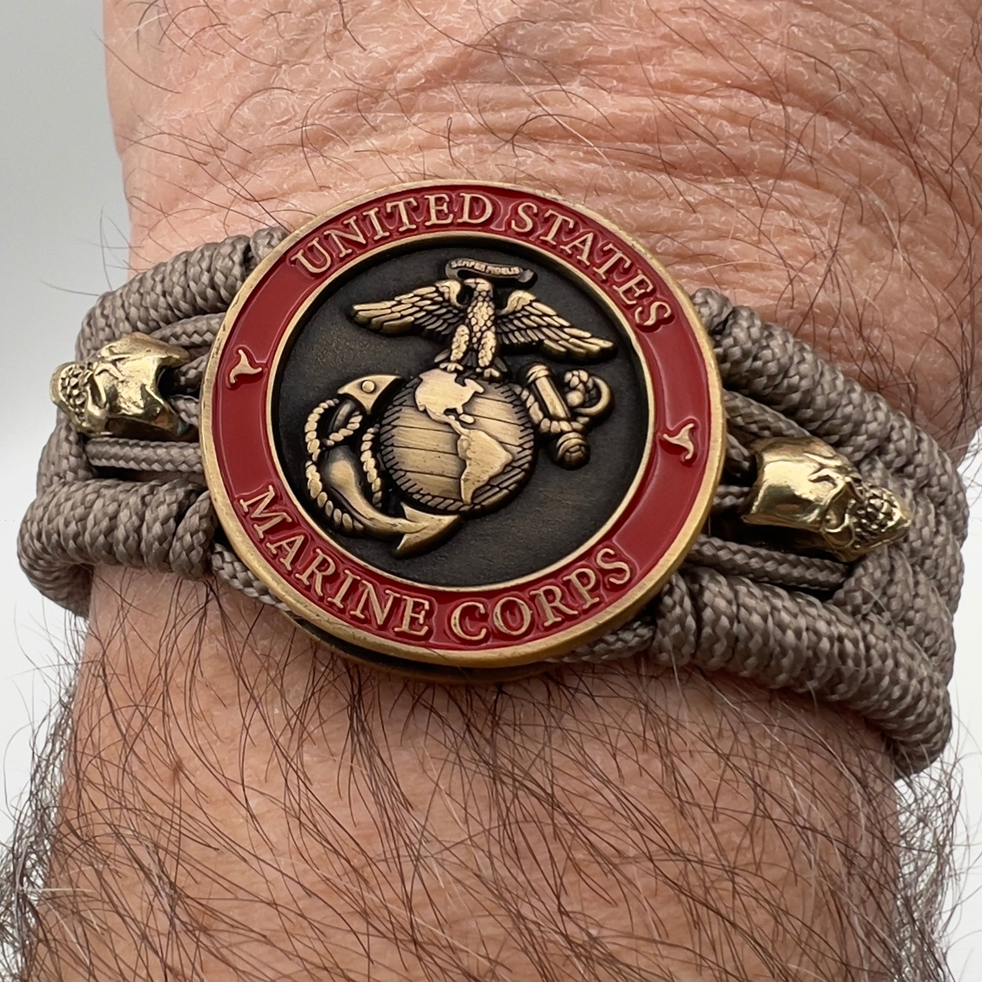 Thin, medium width, flexible and comfortable braided United States Marine Corps bracelet featuring a 24K antique gold plated USMC officer Eagle Globe and Anchor medallion, two gold plated skulls, a gold Cobra style tactical buckle and woven with tan Type-1 paracord.
