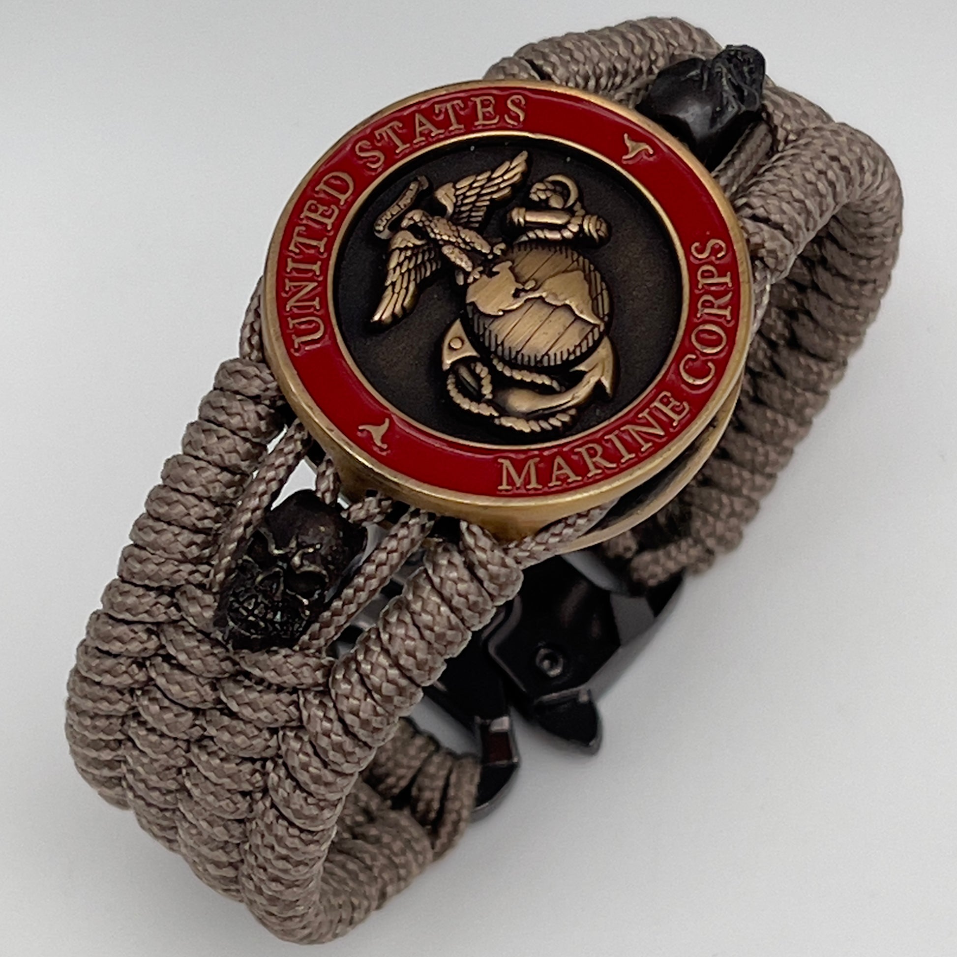 Thin, medium width, flexible and comfortable braided United States Marine Corps bracelet featuring a 24K antique gold plated USMC officer Eagle Globe and Anchor medallion, two black skulls, a black Cobra style tactical buckle and woven with tan Type-1 paracord.
