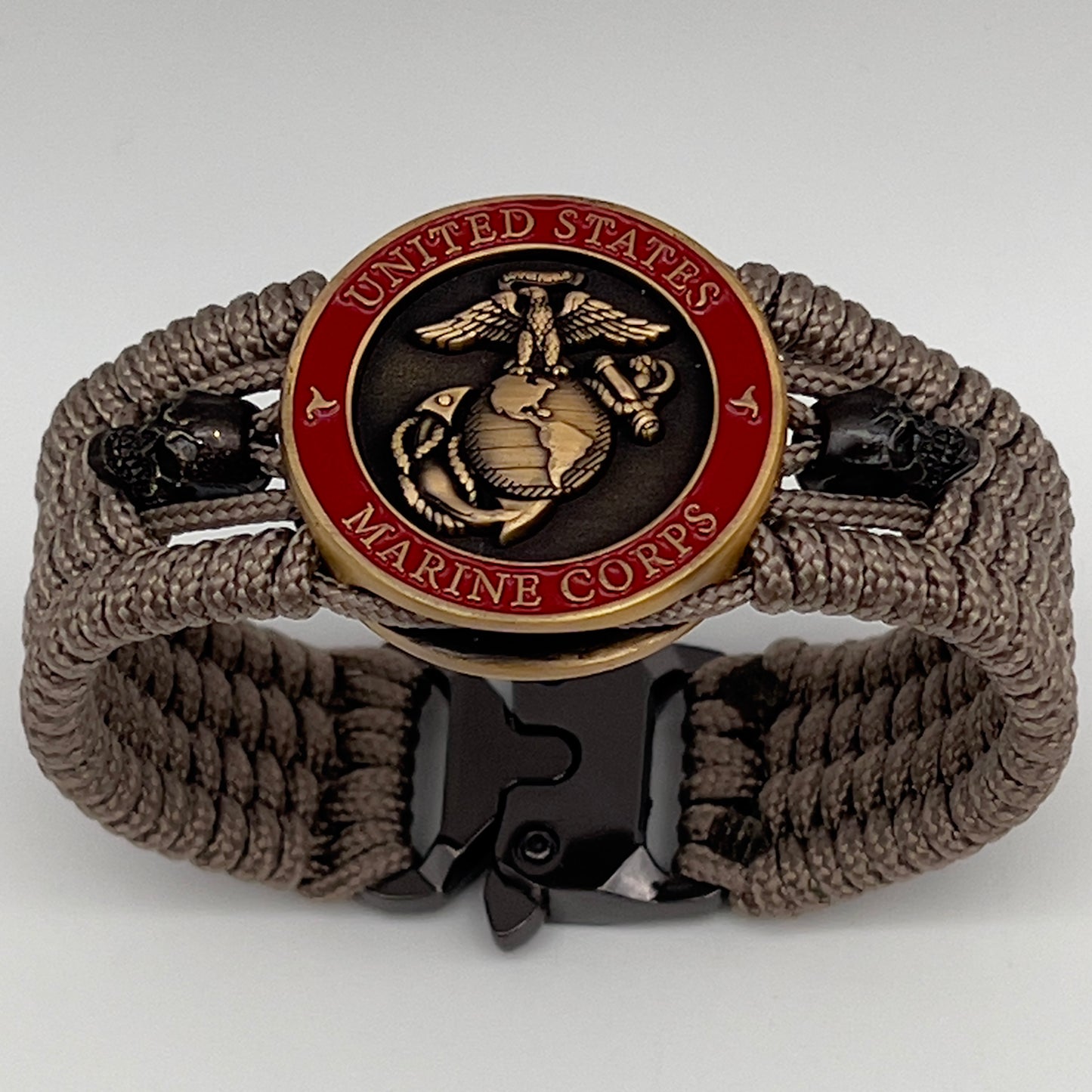 Thin, medium width, flexible and comfortable braided United States Marine Corps bracelet featuring a 24K antique gold plated USMC officer Eagle Globe and Anchor medallion, two black skulls, a black Cobra style tactical buckle and woven with tan Type-1 paracord.