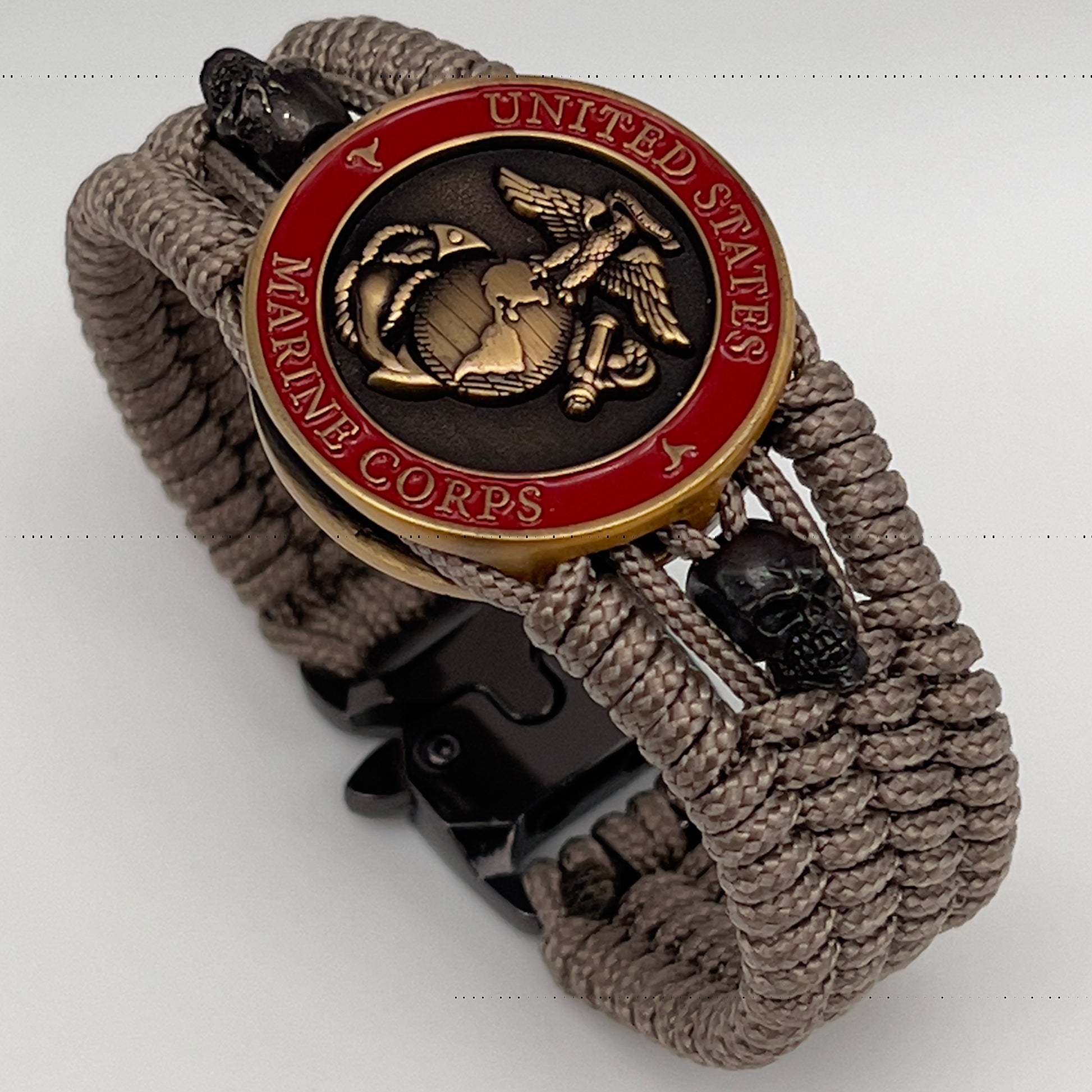 Thin, medium width, flexible and comfortable braided United States Marine Corps bracelet featuring a 24K antique gold plated USMC officer Eagle Globe and Anchor medallion, two black skulls, a black Cobra style tactical buckle and woven with tan Type-1 paracord.