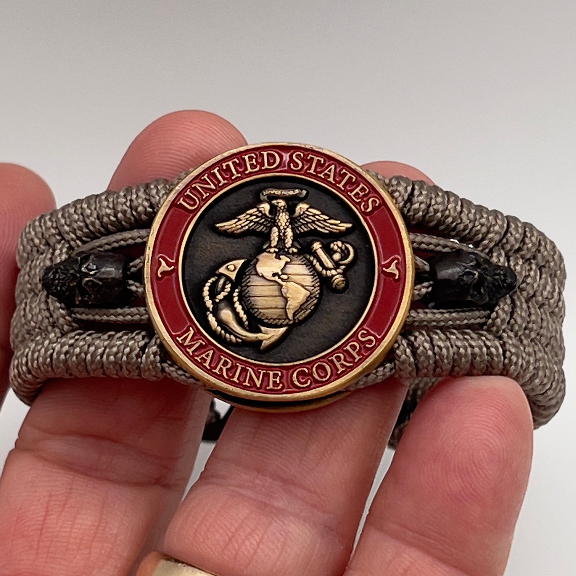 Thin, medium width, flexible and comfortable braided United States Marine Corps bracelet featuring a 24K antique gold plated USMC officer Eagle Globe and Anchor medallion, two black skulls, a black Cobra style tactical buckle and woven with tan Type-1 paracord.
