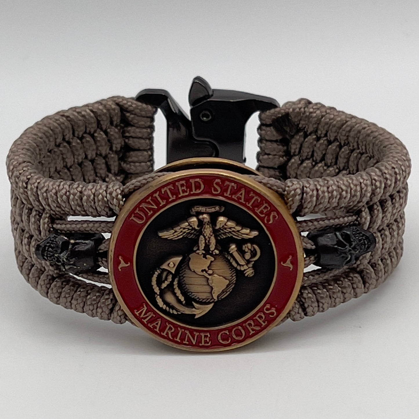 Thin, medium width, flexible and comfortable braided United States Marine Corps bracelet featuring a 24K antique gold plated USMC officer Eagle Globe and Anchor medallion, two black skulls, a black Cobra style tactical buckle and woven with tan Type-1 paracord.