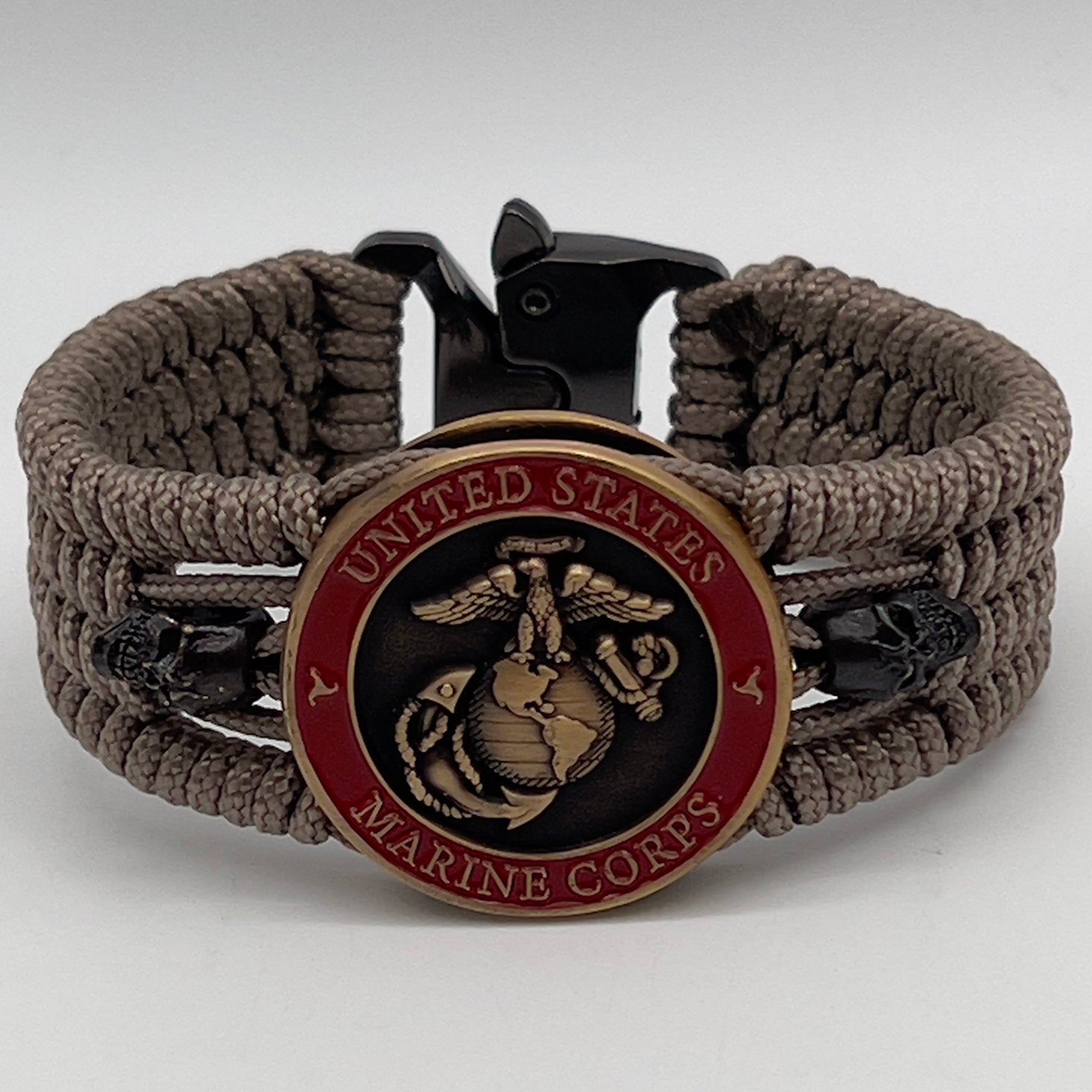 Thin, medium width, flexible and comfortable braided United States Marine Corps bracelet featuring a 24K antique gold plated USMC officer Eagle Globe and Anchor medallion, two black skulls, a black Cobra style tactical buckle and woven with tan Type-1 paracord.
