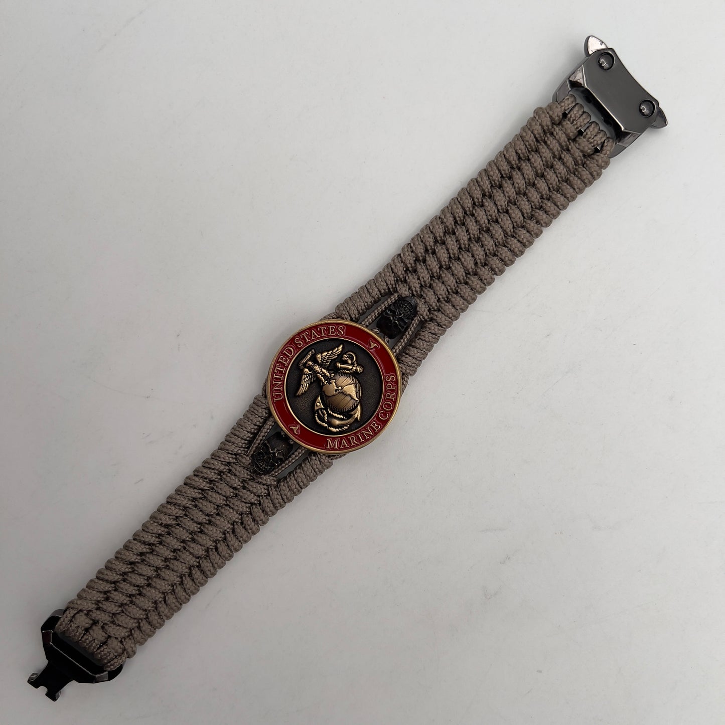 Thin, medium width, flexible and comfortable braided United States Marine Corps bracelet featuring a 24K antique gold plated USMC officer Eagle Globe and Anchor medallion, two black skulls, a black Cobra style tactical buckle and woven with tan Type-1 paracord.