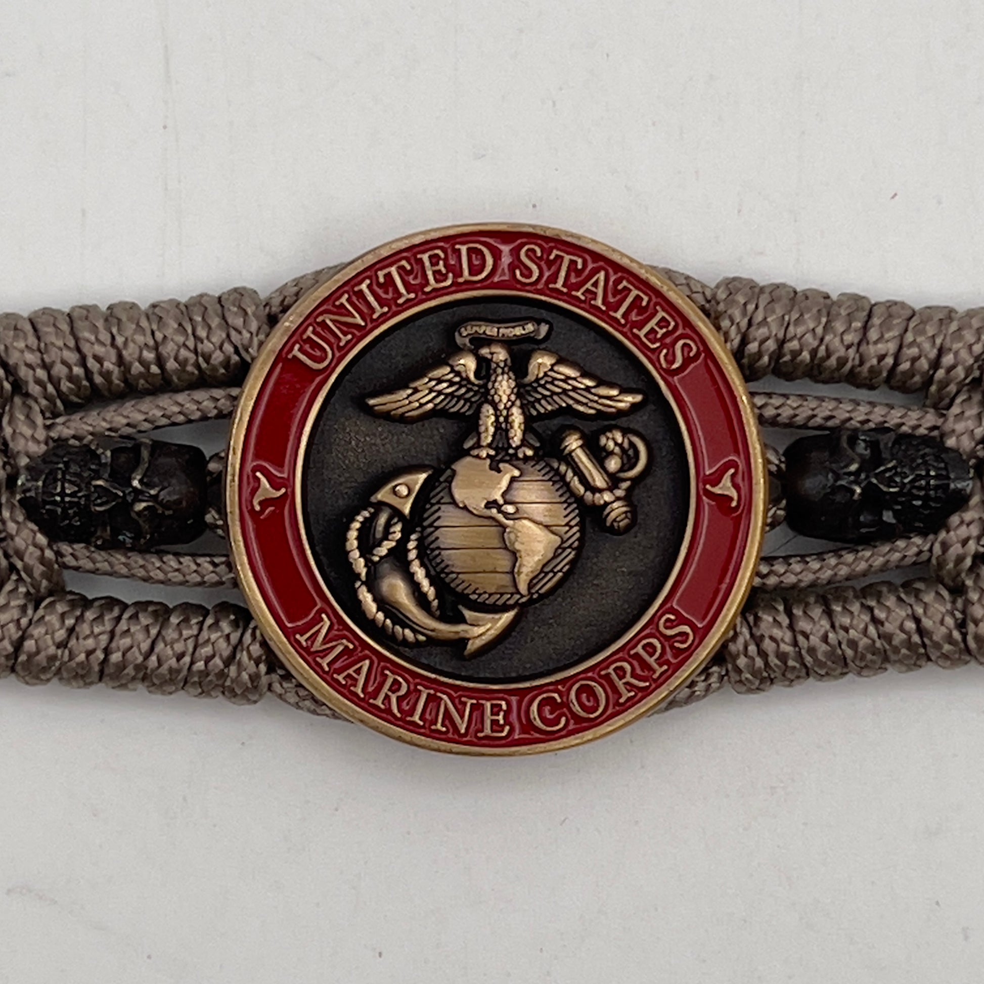 Thin, medium width, flexible and comfortable braided United States Marine Corps bracelet featuring a 24K antique gold plated USMC officer Eagle Globe and Anchor medallion, two black skulls, a black Cobra style tactical buckle and woven with tan Type-1 paracord.