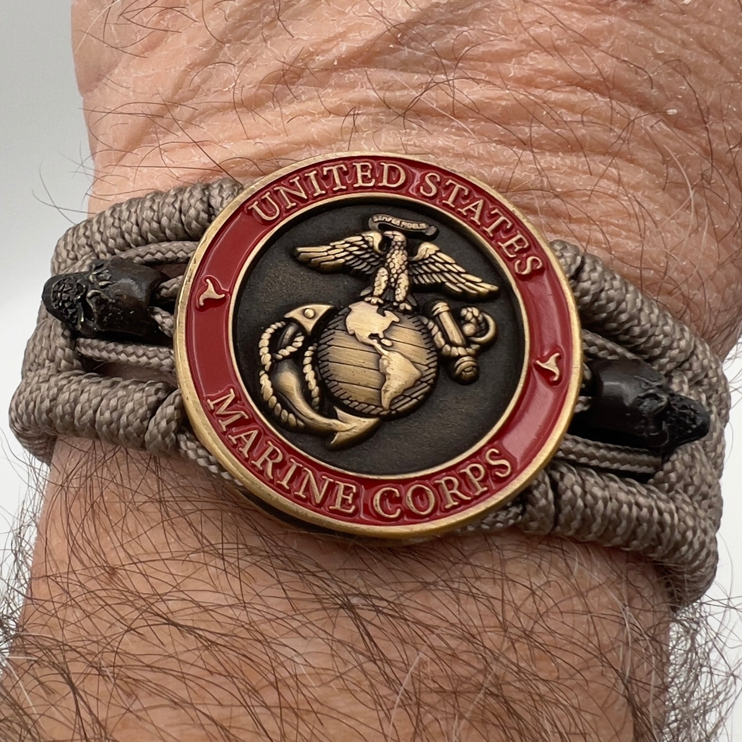 Thin, medium width, flexible and comfortable braided United States Marine Corps bracelet featuring a 24K antique gold plated USMC officer Eagle Globe and Anchor medallion, two black skulls, a black Cobra style tactical buckle and woven with tan Type-1 paracord.