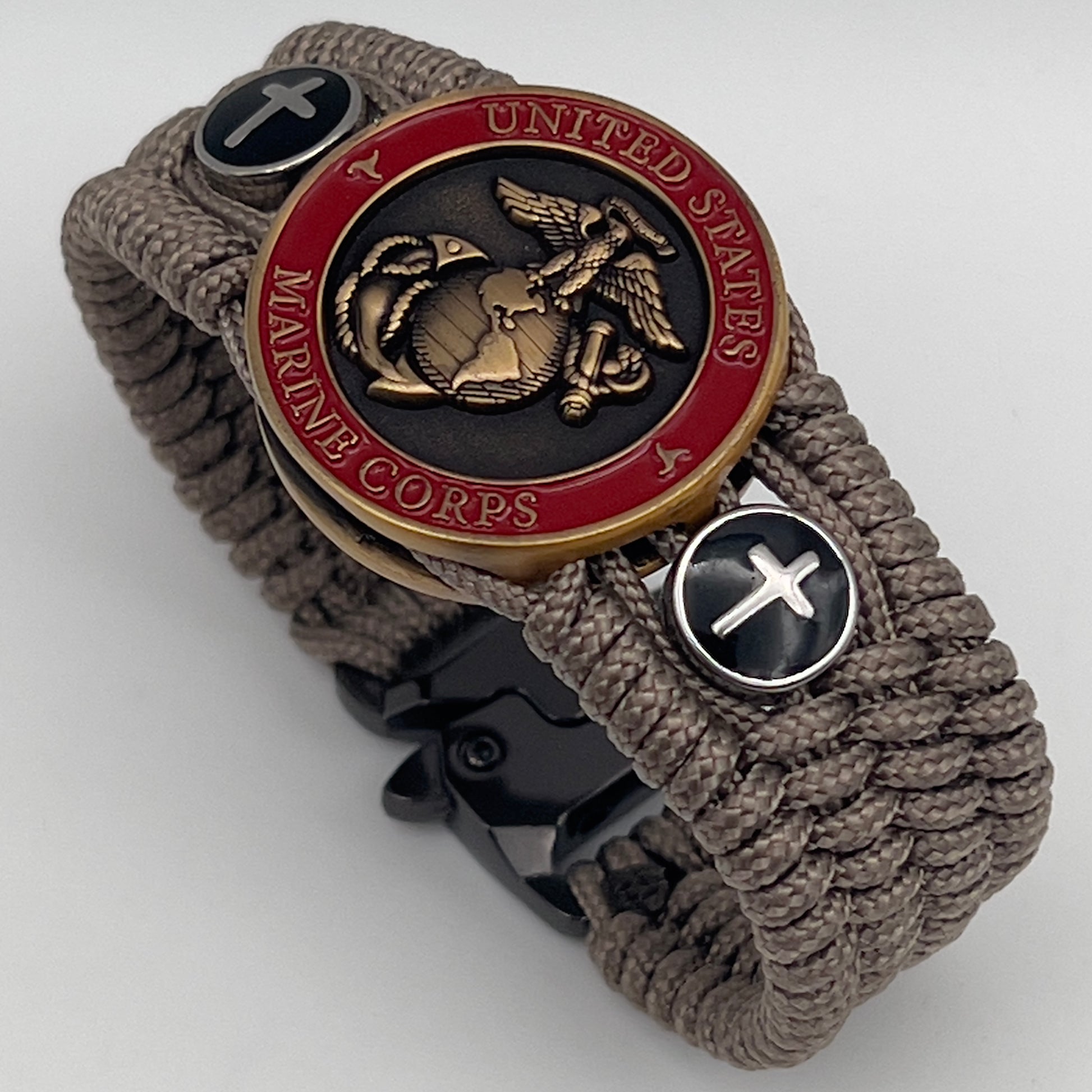 Thin, medium width, flexible and comfortable braided United States Marine Corps bracelet featuring a 24K antique gold plated USMC officer Eagle Globe and Anchor medallion, two Christian crosses, a black Cobra style tactical buckle and woven with Tan Type-1 paracord.