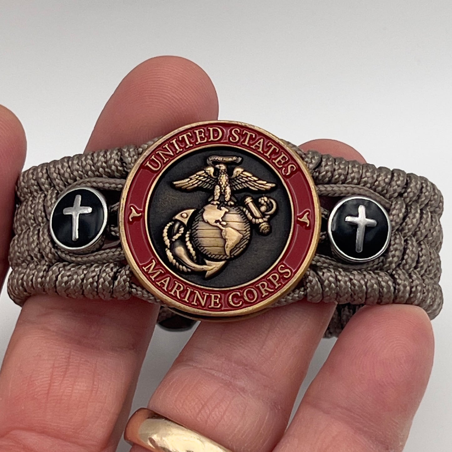 Thin, medium width, flexible and comfortable braided United States Marine Corps bracelet featuring a 24K antique gold plated USMC officer Eagle Globe and Anchor medallion, two Christian crosses, a black Cobra style tactical buckle and woven with Tan Type-1 paracord.