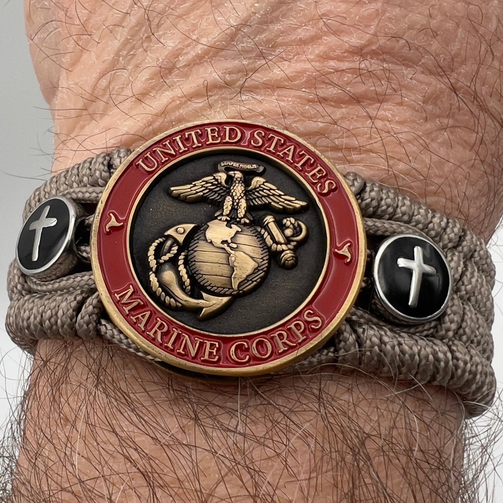 Thin, medium width, flexible and comfortable braided United States Marine Corps bracelet featuring a 24K antique gold plated USMC officer Eagle Globe and Anchor medallion, two Christian crosses, a black Cobra style tactical buckle and woven with Tan Type-1 paracord.