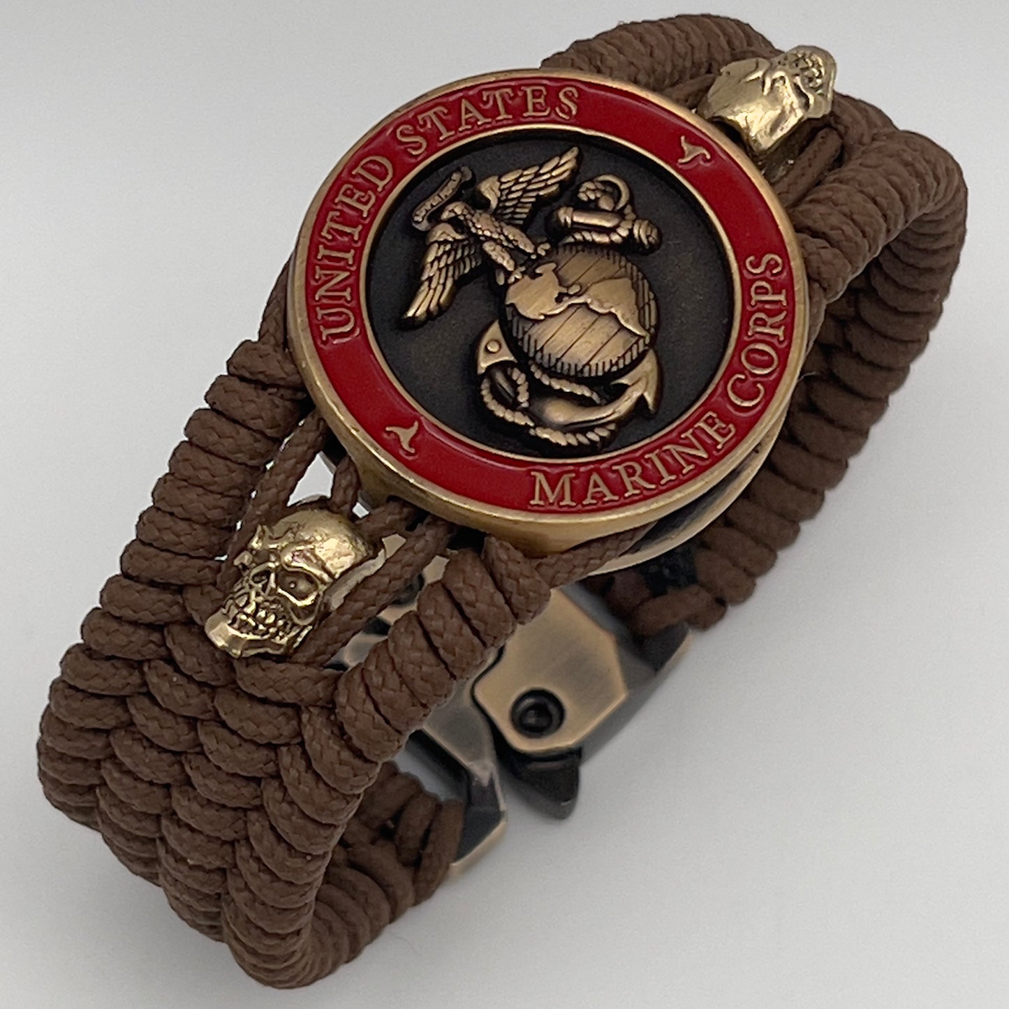 Thin, medium width, flexible and comfortable braided United States Marine Corps bracelet featuring a 24K antique gold plated USMC officer Eagle Globe and Anchor medallion, two gold plated skulls, a gold Cobra style tactical buckle and woven with Coyote Brown Type-1 paracord.