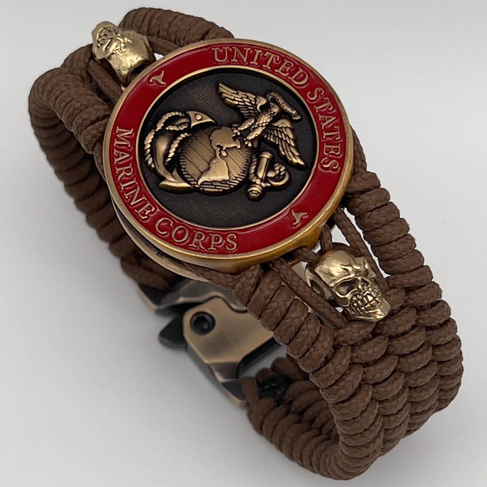 Thin, medium width, flexible and comfortable braided United States Marine Corps bracelet featuring a 24K antique gold plated USMC officer Eagle Globe and Anchor medallion, two gold plated skulls, a gold Cobra style tactical buckle and woven with Coyote Brown Type-1 paracord.