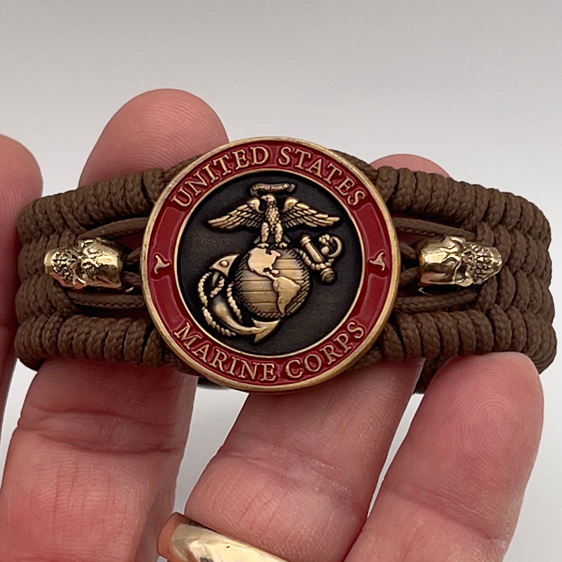 Thin, medium width, flexible and comfortable braided United States Marine Corps bracelet featuring a 24K antique gold plated USMC officer Eagle Globe and Anchor medallion, two gold plated skulls, a gold Cobra style tactical buckle and woven with Coyote Brown Type-1 paracord.