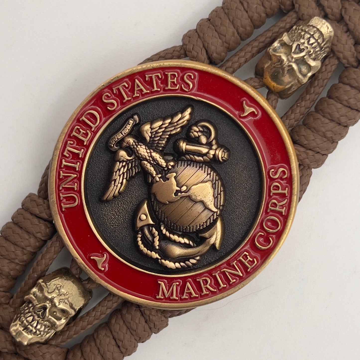 Thin, medium width, flexible and comfortable braided United States Marine Corps bracelet featuring a 24K antique gold plated USMC officer Eagle Globe and Anchor medallion, two gold plated skulls, a gold Cobra style tactical buckle and woven with Coyote Brown Type-1 paracord.