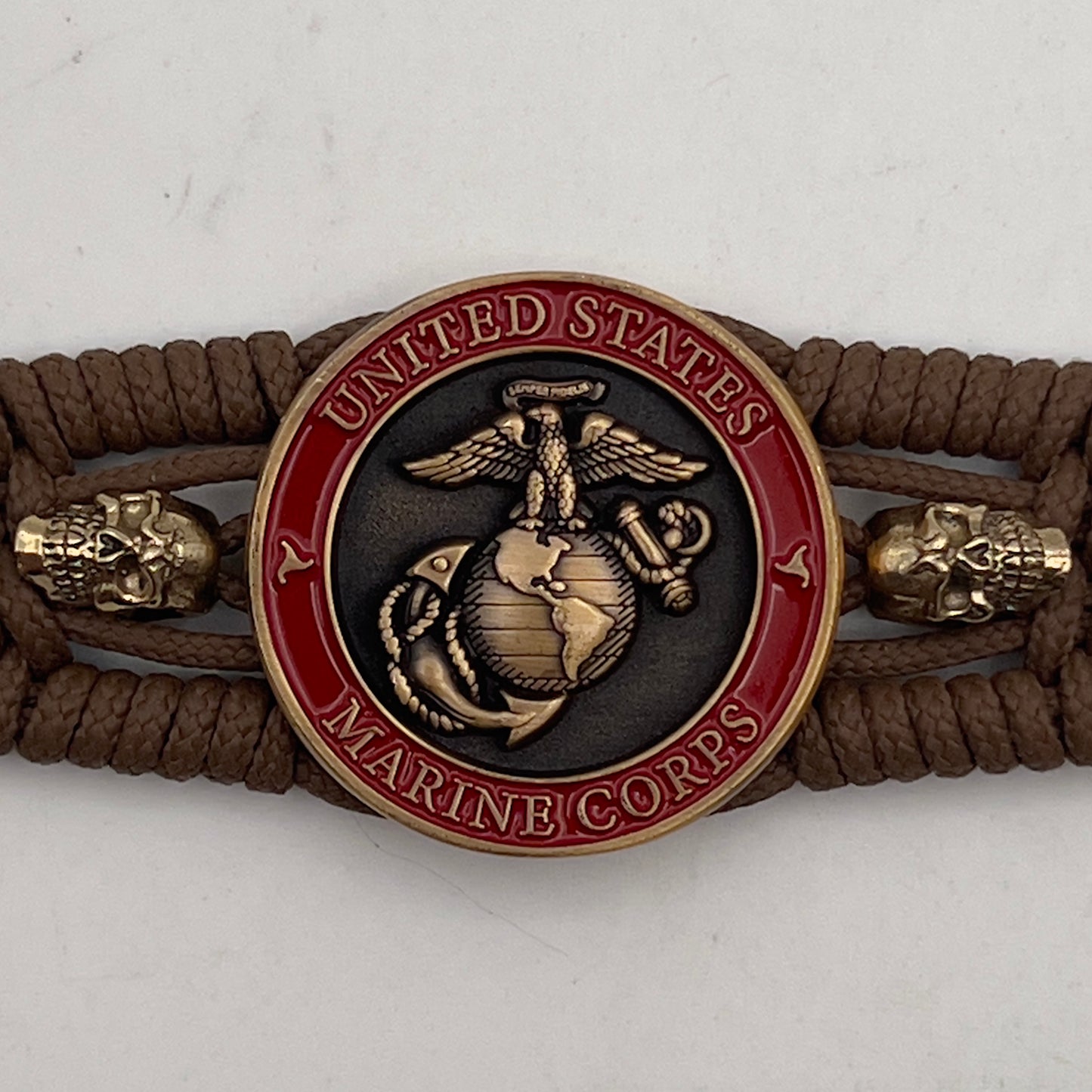 Thin, medium width, flexible and comfortable braided United States Marine Corps bracelet featuring a 24K antique gold plated USMC officer Eagle Globe and Anchor medallion, two gold plated skulls, a gold Cobra style tactical buckle and woven with Coyote Brown Type-1 paracord.
