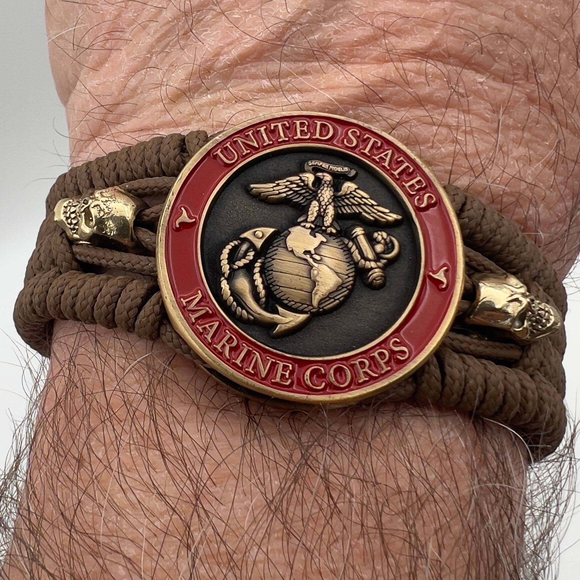 Thin, medium width, flexible and comfortable braided United States Marine Corps bracelet featuring a 24K antique gold plated USMC officer Eagle Globe and Anchor medallion, two gold plated skulls, a gold Cobra style tactical buckle and woven with Coyote Brown Type-1 paracord.