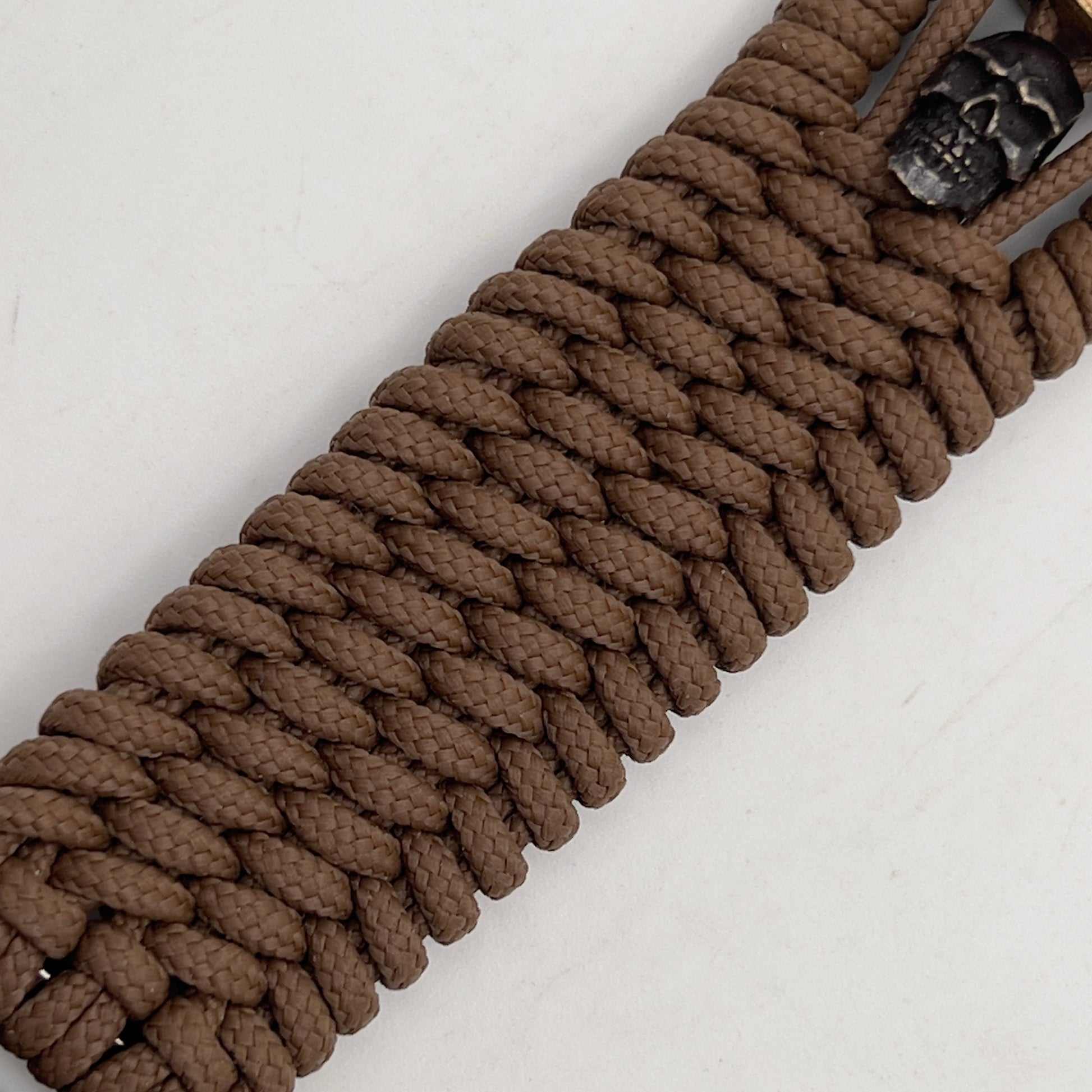 Thin, medium width, flexible and comfortable braided United States Marine Corps bracelet featuring a 24K antique gold plated USMC officer Eagle Globe and Anchor medallion, two black skulls, a black Cobra style tactical buckle and woven with Coyote Brown Type-1 paracord.