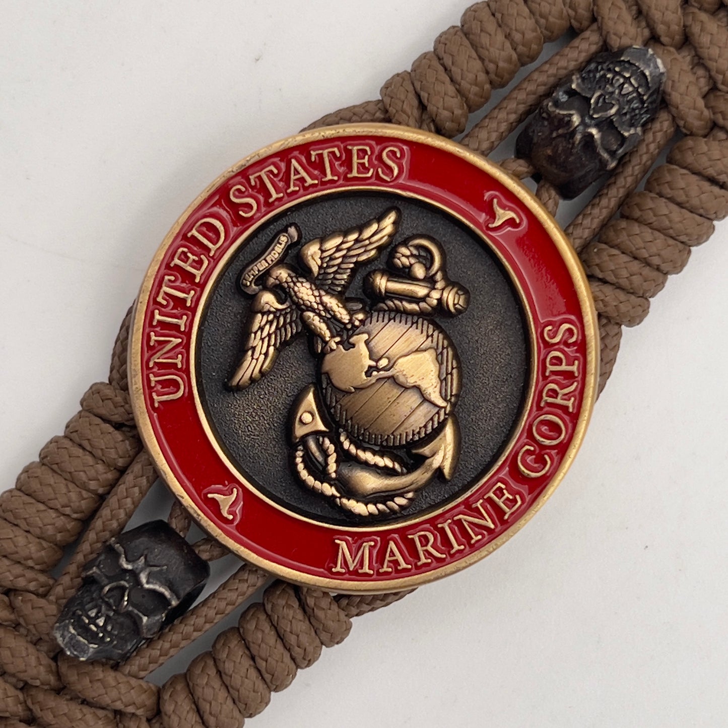 Thin, medium width, flexible and comfortable braided United States Marine Corps bracelet featuring a 24K antique gold plated USMC officer Eagle Globe and Anchor medallion, two black skulls, a black Cobra style tactical buckle and woven with Coyote Brown Type-1 paracord.