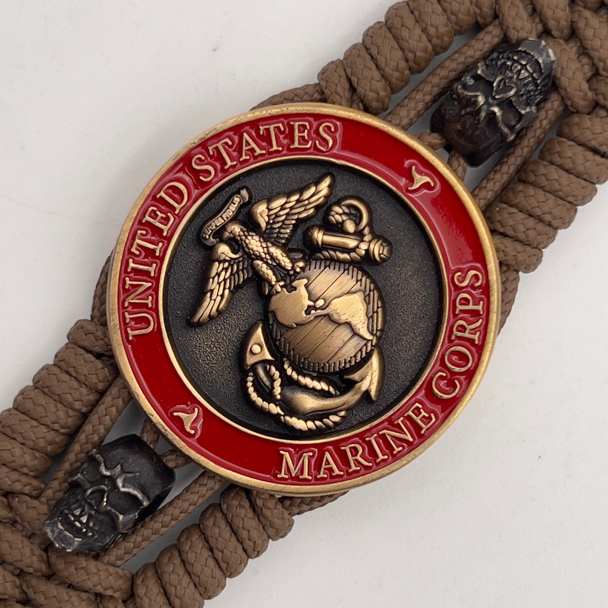 Thin, medium width, flexible and comfortable braided United States Marine Corps bracelet featuring a 24K antique gold plated USMC officer Eagle Globe and Anchor medallion, two black skulls, a black Cobra style tactical buckle and woven with Coyote Brown Type-1 paracord.