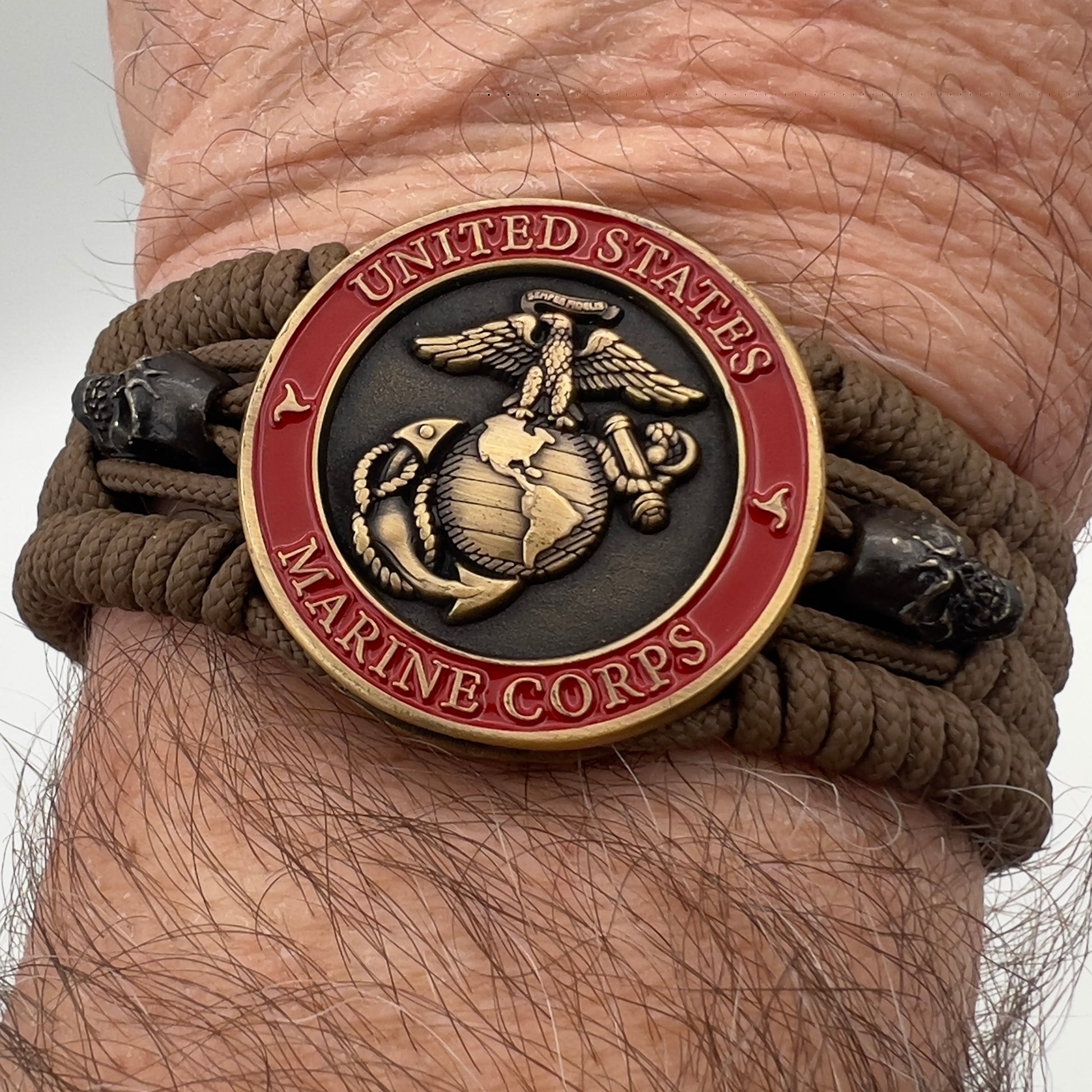 Thin, medium width, flexible and comfortable braided United States Marine Corps bracelet featuring a 24K antique gold plated USMC officer Eagle Globe and Anchor medallion, two black skulls, a black Cobra style tactical buckle and woven with Coyote Brown Type-1 paracord.