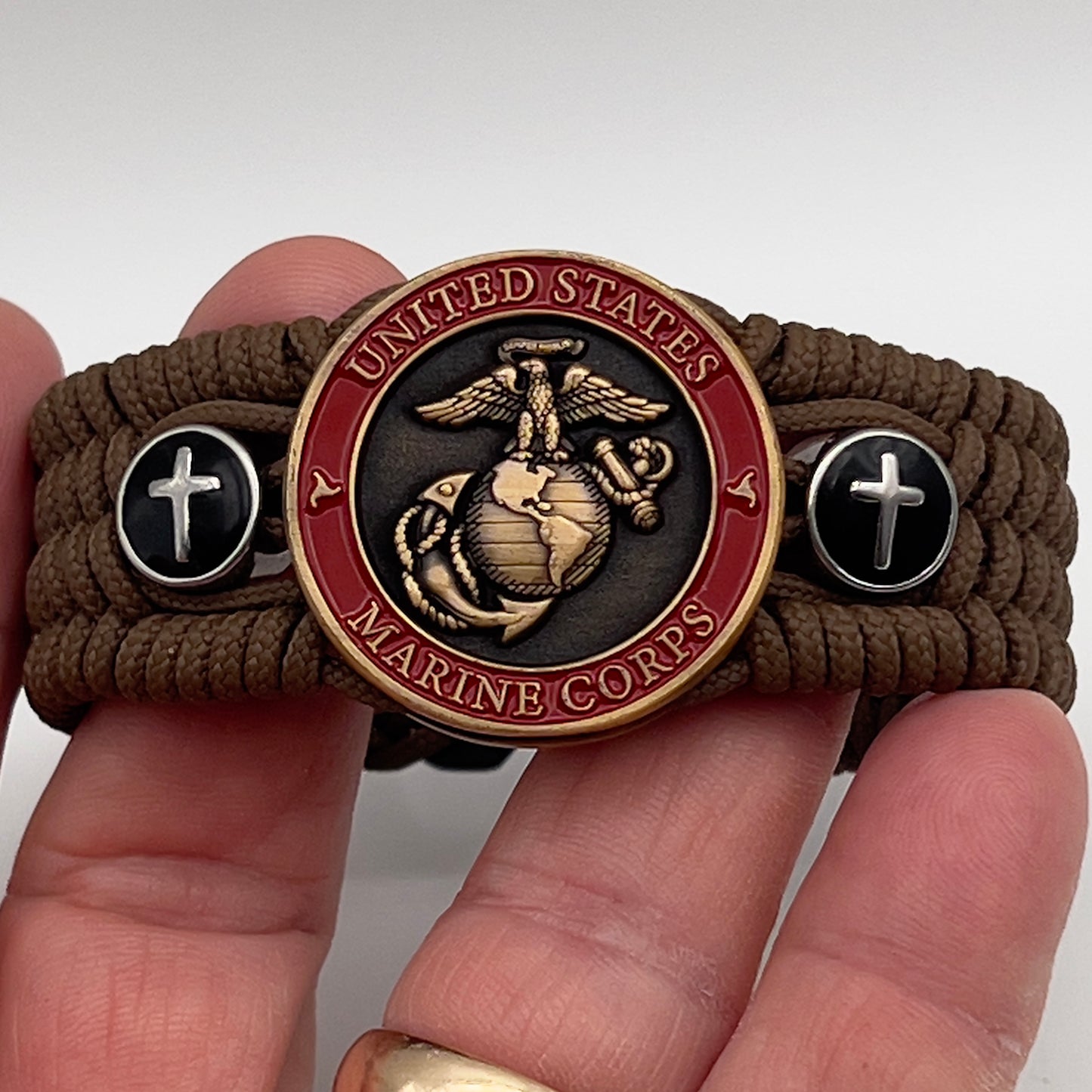 Thin, medium width, flexible and comfortable braided United States Marine Corps bracelet featuring a 24K antique gold plated USMC officer Eagle Globe and Anchor medallion, two Christian crosses, a black Cobra style tactical buckle and woven with Coyote Brown Type-1 paracord.