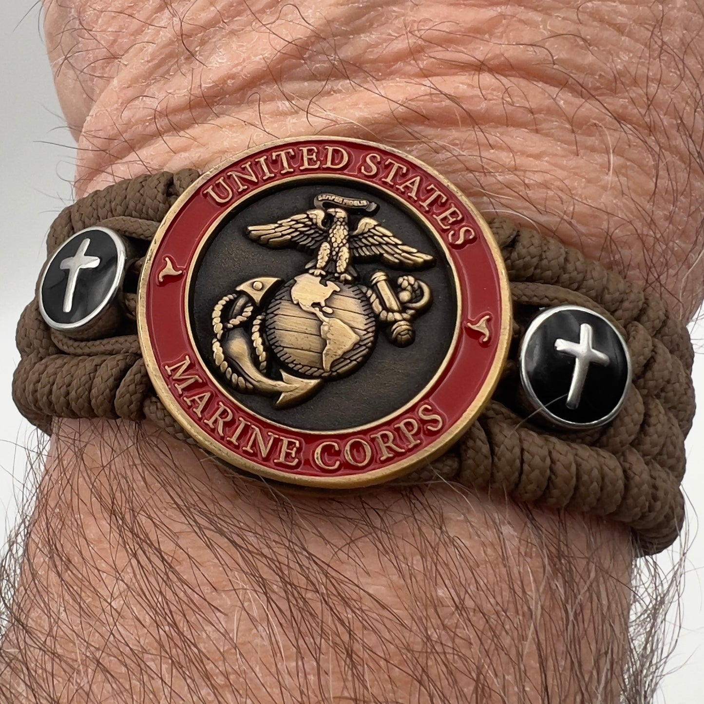 Thin, medium width, flexible and comfortable braided United States Marine Corps bracelet featuring a 24K antique gold plated USMC officer Eagle Globe and Anchor medallion, two Christian crosses, a black Cobra style tactical buckle and woven with Coyote Brown Type-1 paracord.