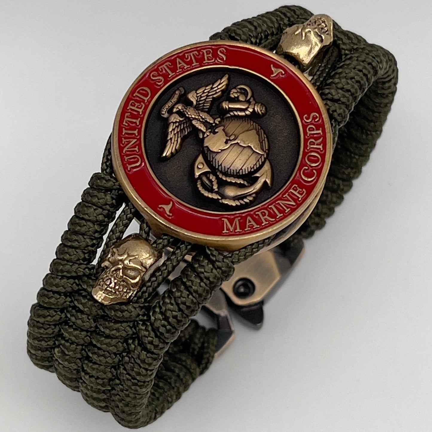 Thin, medium width, flexible and comfortable braided United States Marine Corps bracelet featuring a 24K antique gold plated USMC officer Eagle Globe and Anchor medallion, two gold plated skulls, a gold Cobra style tactical buckle and woven with Olive Drab Type-1 paracord.