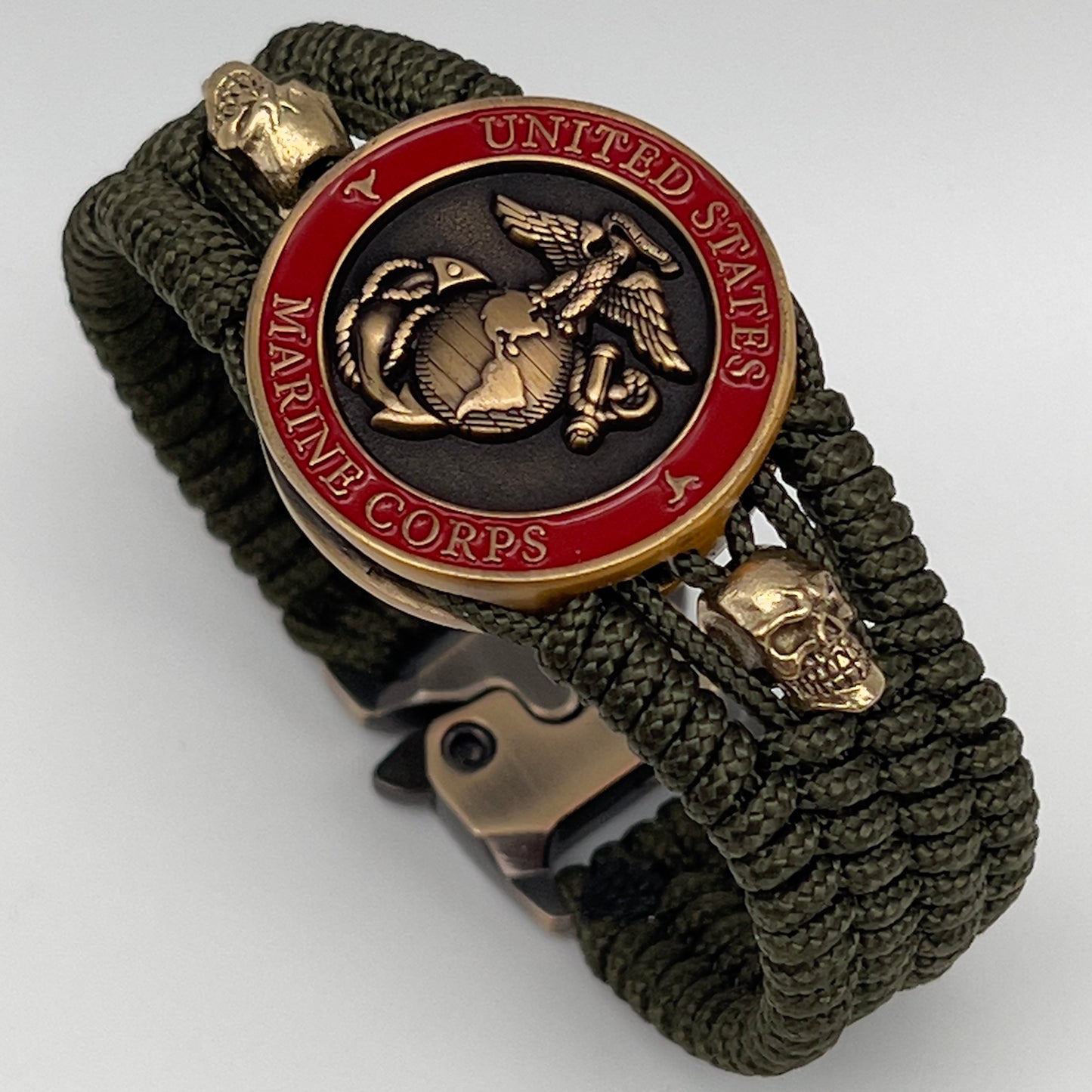 Thin, medium width, flexible and comfortable braided United States Marine Corps bracelet featuring a 24K antique gold plated USMC officer Eagle Globe and Anchor medallion, two gold plated skulls, a gold Cobra style tactical buckle and woven with Olive Drab Type-1 paracord.