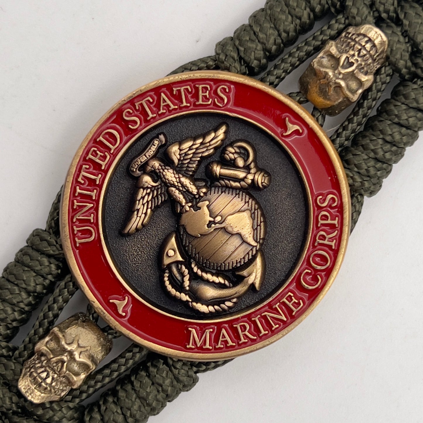 Thin, medium width, flexible and comfortable braided United States Marine Corps bracelet featuring a 24K antique gold plated USMC officer Eagle Globe and Anchor medallion, two gold plated skulls, a gold Cobra style tactical buckle and woven with Olive Drab Type-1 paracord.