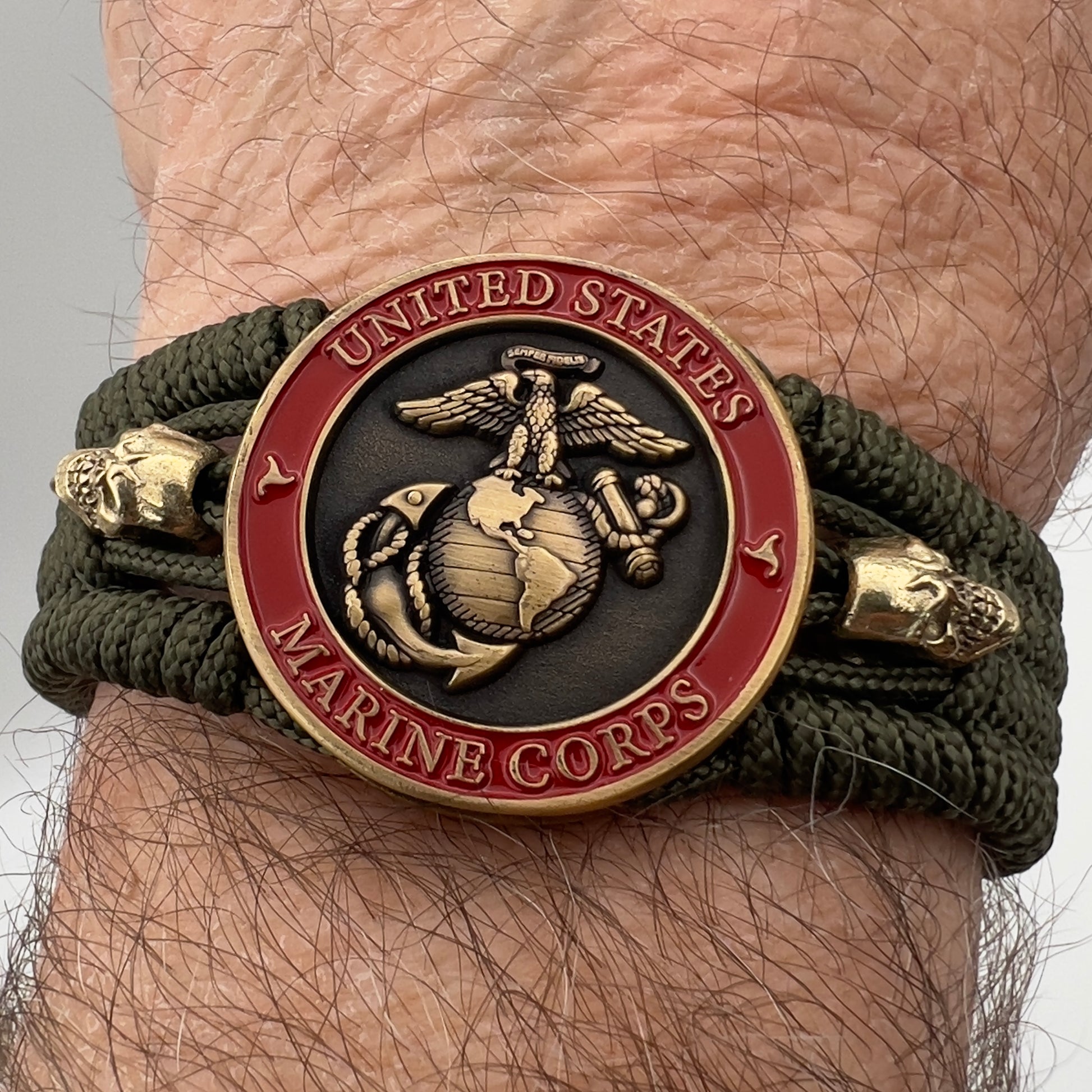 Thin, medium width, flexible and comfortable braided United States Marine Corps bracelet featuring a 24K antique gold plated USMC officer Eagle Globe and Anchor medallion, two gold plated skulls, a gold Cobra style tactical buckle and woven with Olive Drab Type-1 paracord.