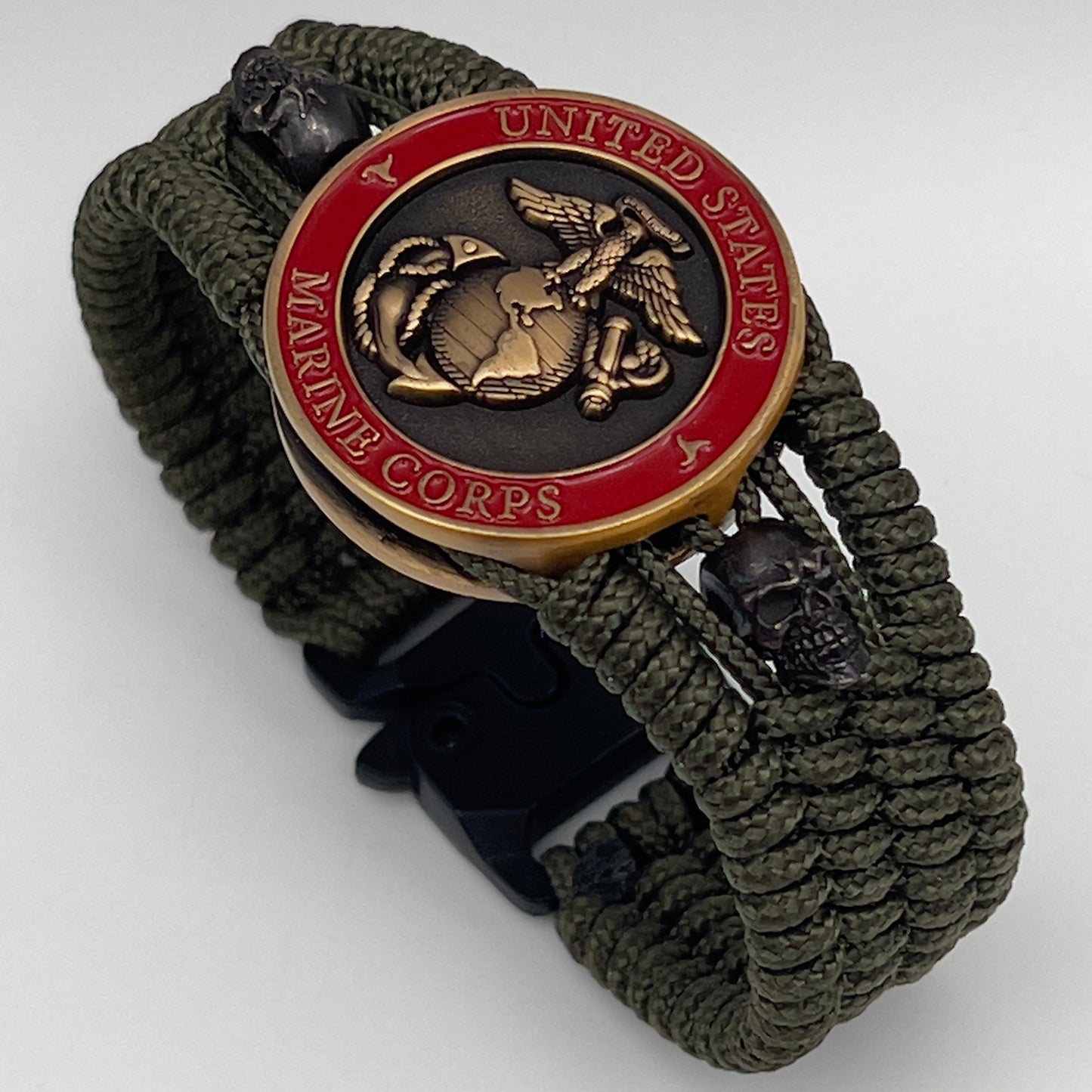 Thin, medium width, flexible and comfortable braided United States Marine Corps bracelet featuring a 24K antique gold plated USMC officer Eagle Globe and Anchor medallion, two black skulls, a black Cobra style tactical buckle and woven with Olive Drab Type-1 paracord.