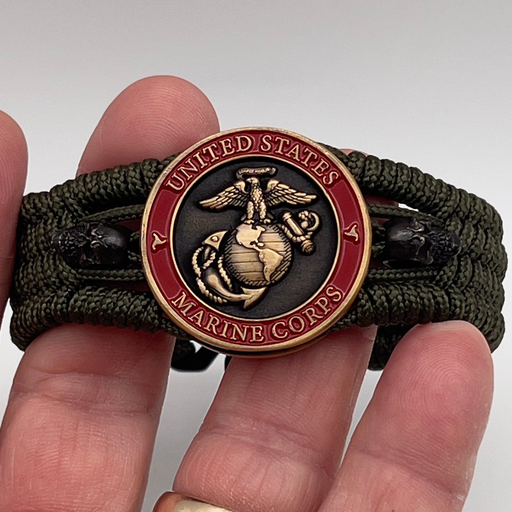 Thin, medium width, flexible and comfortable braided United States Marine Corps bracelet featuring a 24K antique gold plated USMC officer Eagle Globe and Anchor medallion, two black skulls, a black Cobra style tactical buckle and woven with Olive Drab Type-1 paracord.