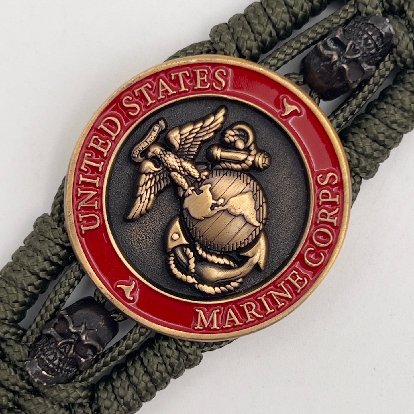 Thin, medium width, flexible and comfortable braided United States Marine Corps bracelet featuring a 24K antique gold plated USMC officer Eagle Globe and Anchor medallion, two black skulls, a black Cobra style tactical buckle and woven with Olive Drab Type-1 paracord.