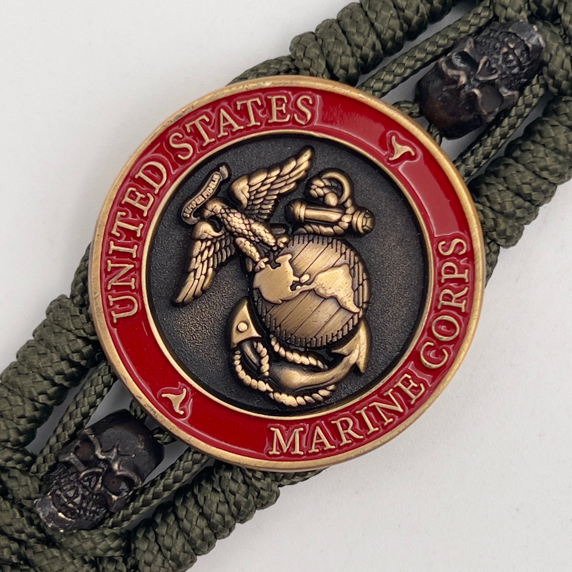 Thin, medium width, flexible and comfortable braided United States Marine Corps bracelet featuring a 24K antique gold plated USMC officer Eagle Globe and Anchor medallion, two black skulls, a black Cobra style tactical buckle and woven with Olive Drab Type-1 paracord.