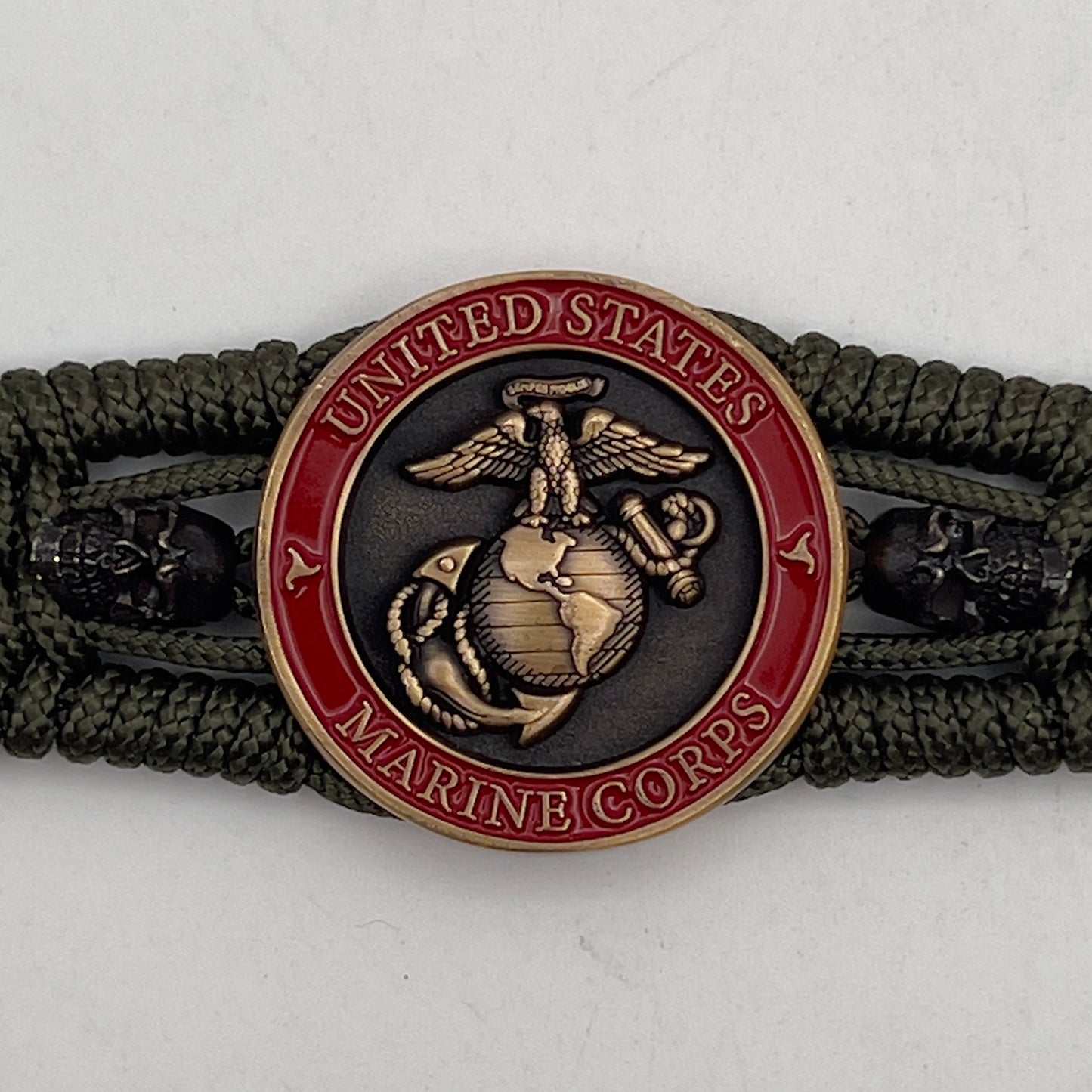 Thin, medium width, flexible and comfortable braided United States Marine Corps bracelet featuring a 24K antique gold plated USMC officer Eagle Globe and Anchor medallion, two black skulls, a black Cobra style tactical buckle and woven with Olive Drab Type-1 paracord.
