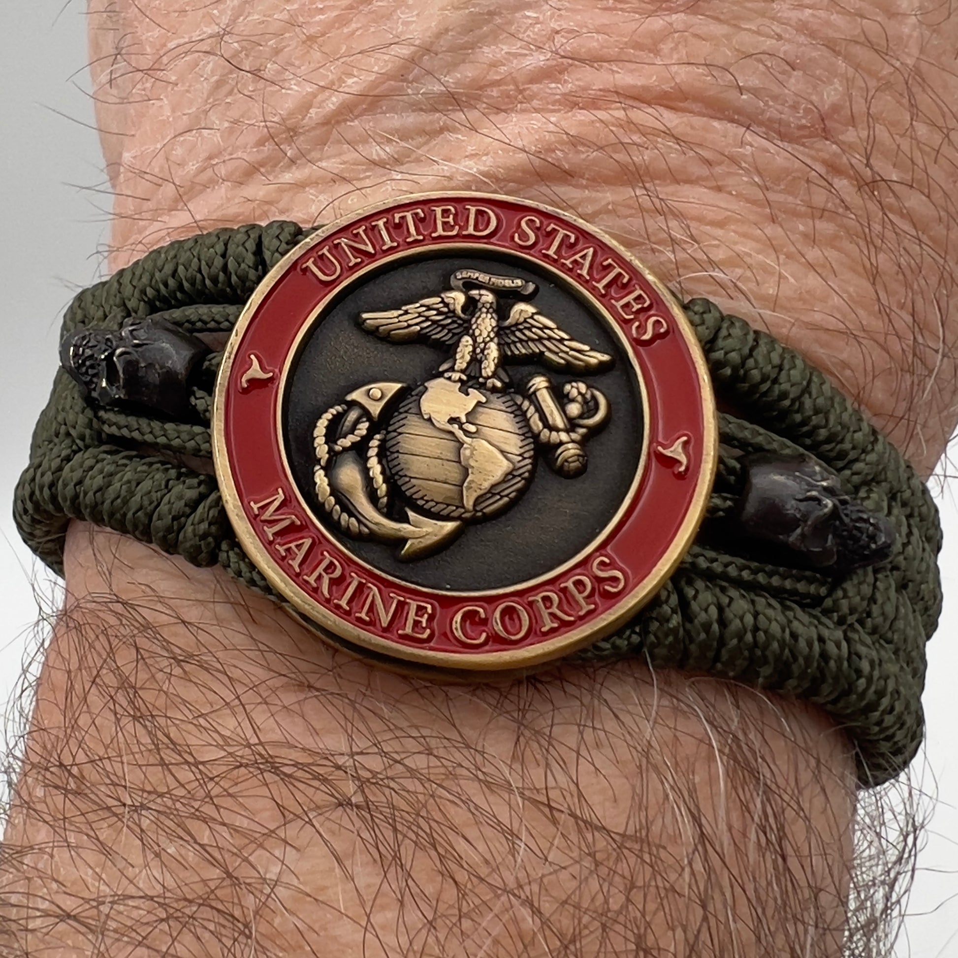 Thin, medium width, flexible and comfortable braided United States Marine Corps bracelet featuring a 24K antique gold plated USMC officer Eagle Globe and Anchor medallion, two black skulls, a black Cobra style tactical buckle and woven with Olive Drab Type-1 paracord.