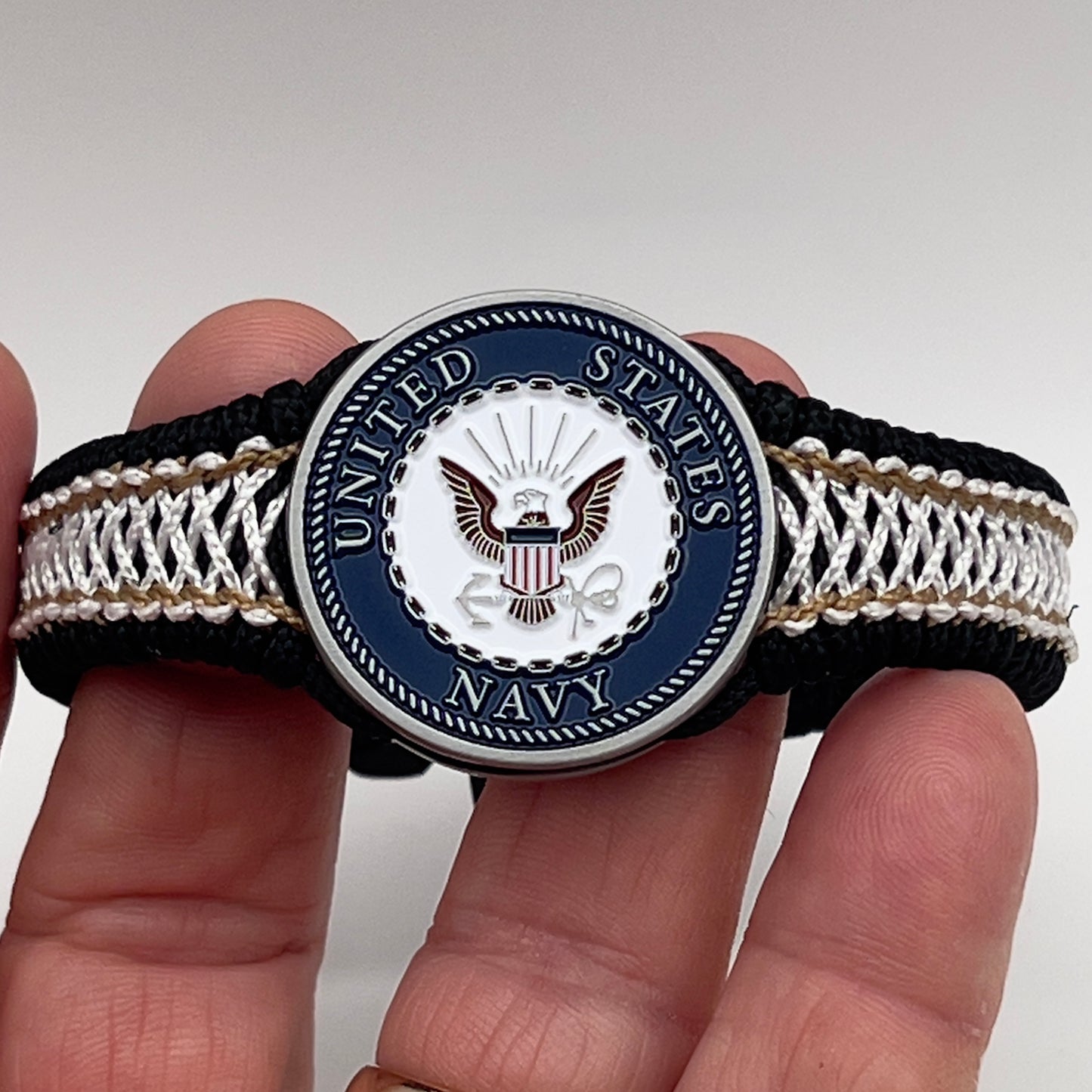 Thin, narrow, flexible and comfortable braided United States Marine Corps bracelet featuring an antique silver plated United States Navy medallion, a black Cobra style tactical buckle and woven with black Type-1 paracord and Gold adn White nano cord.