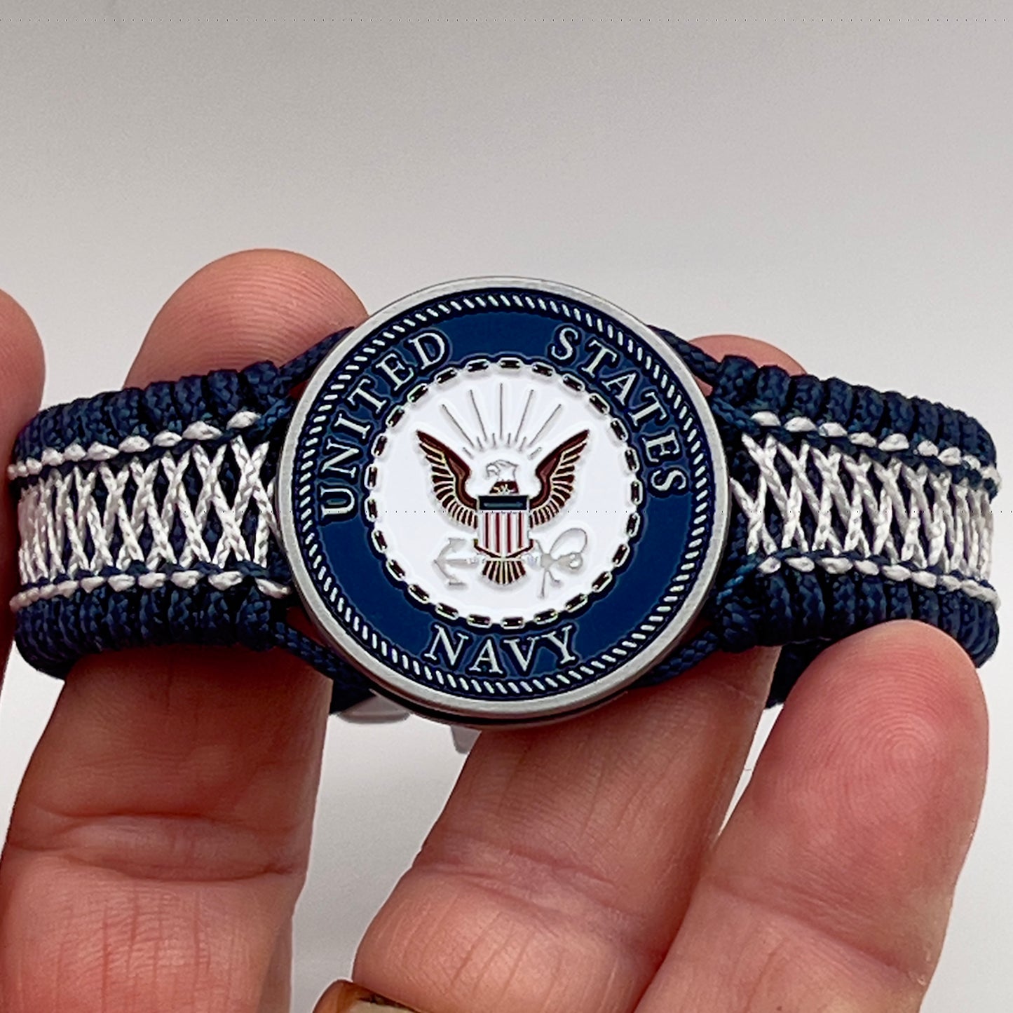 Thin, wide and comfortable braided United States Navy bracelet featuring an antique silver plated Navy medallion, a silver Cobra style tactical buckle and woven with Navy Blue Type-1 paracord and Nay Blue and White nano cord.