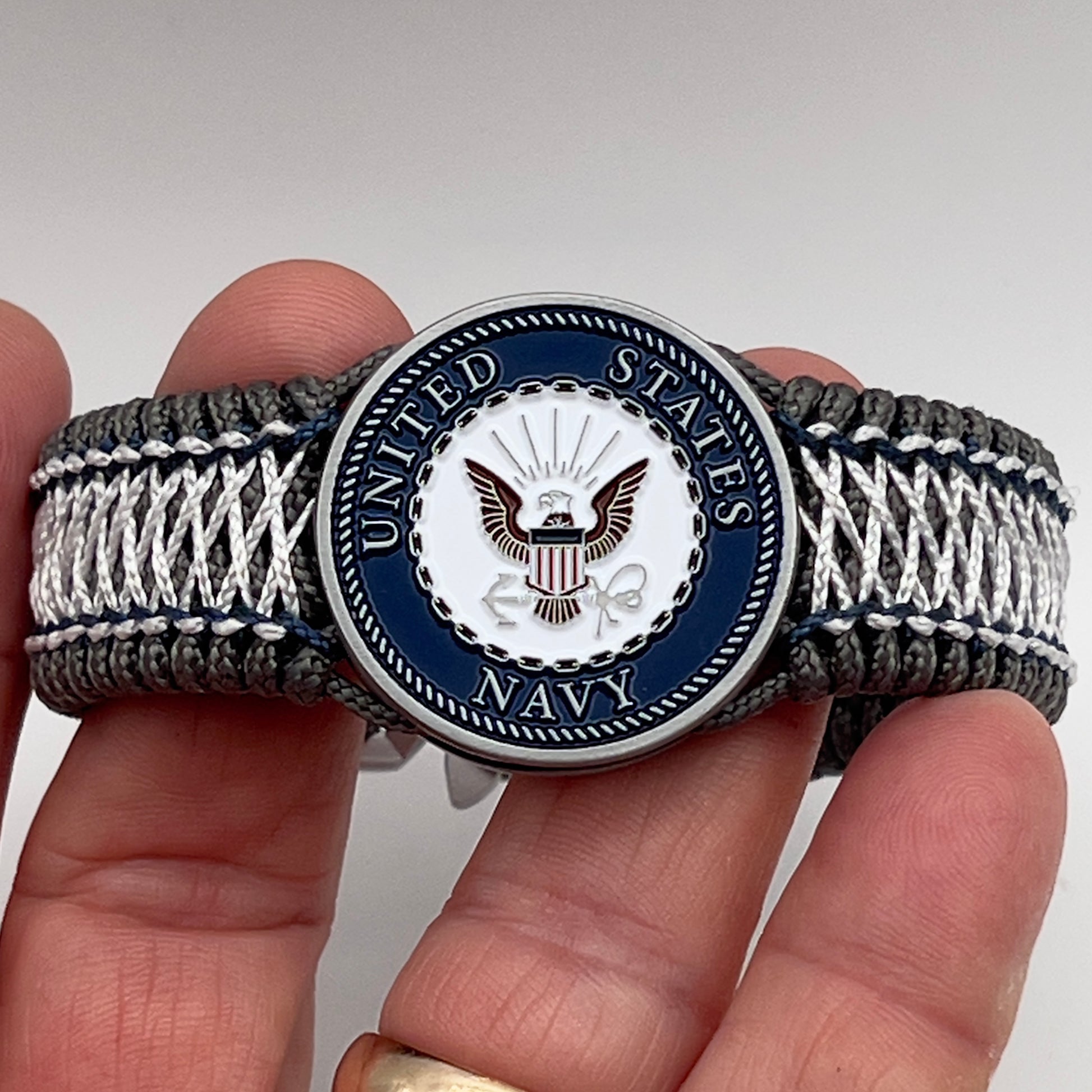 Thin, wide and comfortable braided United States Navy bracelet featuring an antique silver plated Navy medallion, a silver Cobra style tactical buckle and woven with Charcoal Gray Type-1 paracord and Nay Blue and White nano cord.