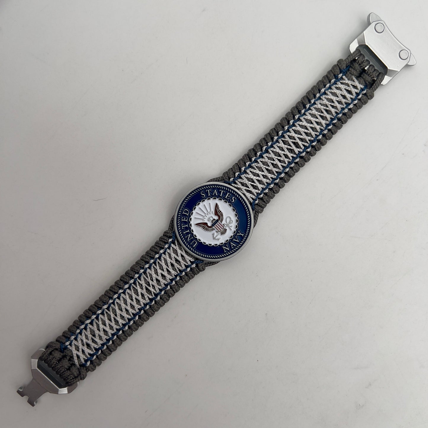 Thin, wide and comfortable braided United States Navy bracelet featuring an antique silver plated Navy medallion, a silver Cobra style tactical buckle and woven with Charcoal Gray Type-1 paracord and Nay Blue and White nano cord.