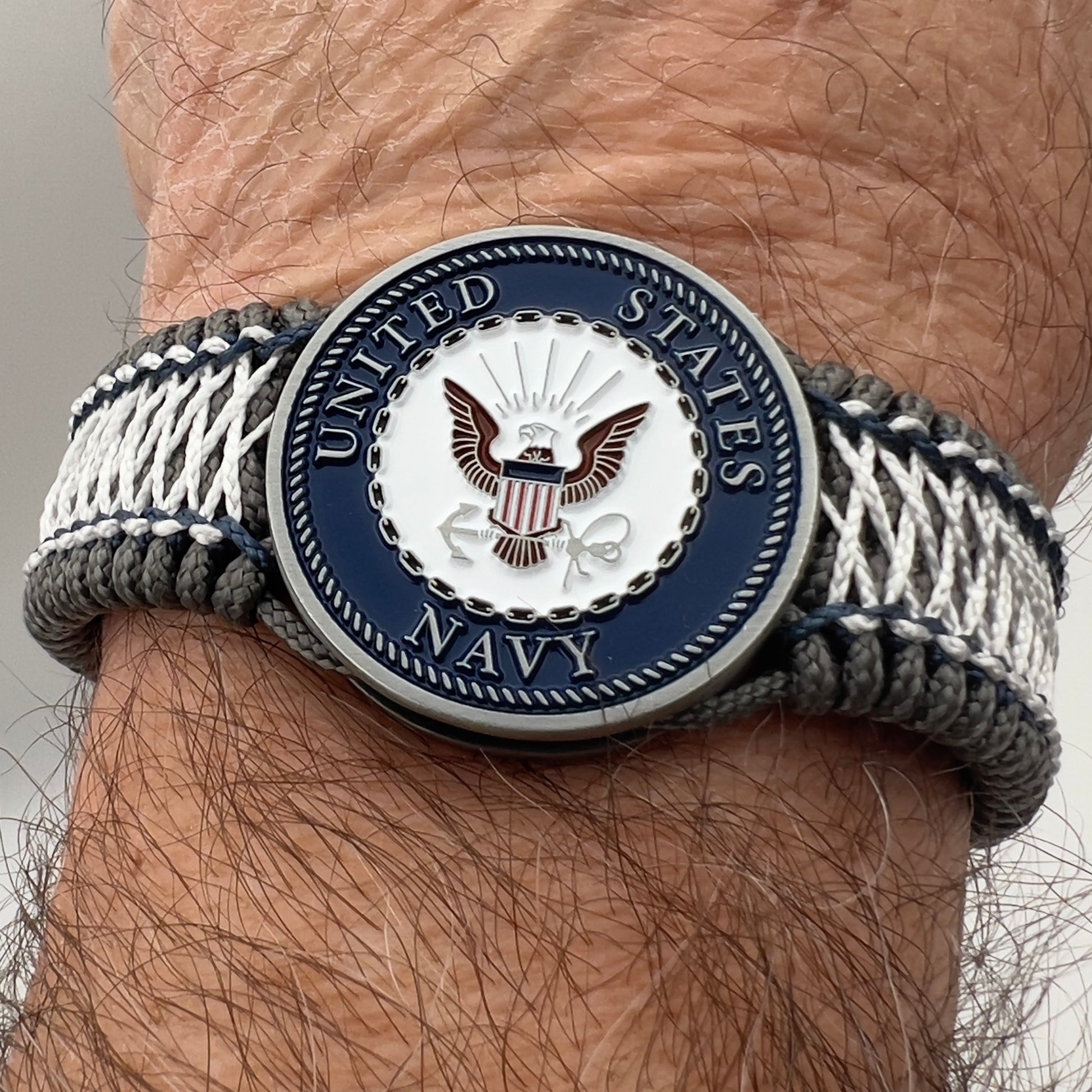 Thin, wide and comfortable braided United States Navy bracelet featuring an antique silver plated Navy medallion, a silver Cobra style tactical buckle and woven with Charcoal Gray Type-1 paracord and Nay Blue and White nano cord.