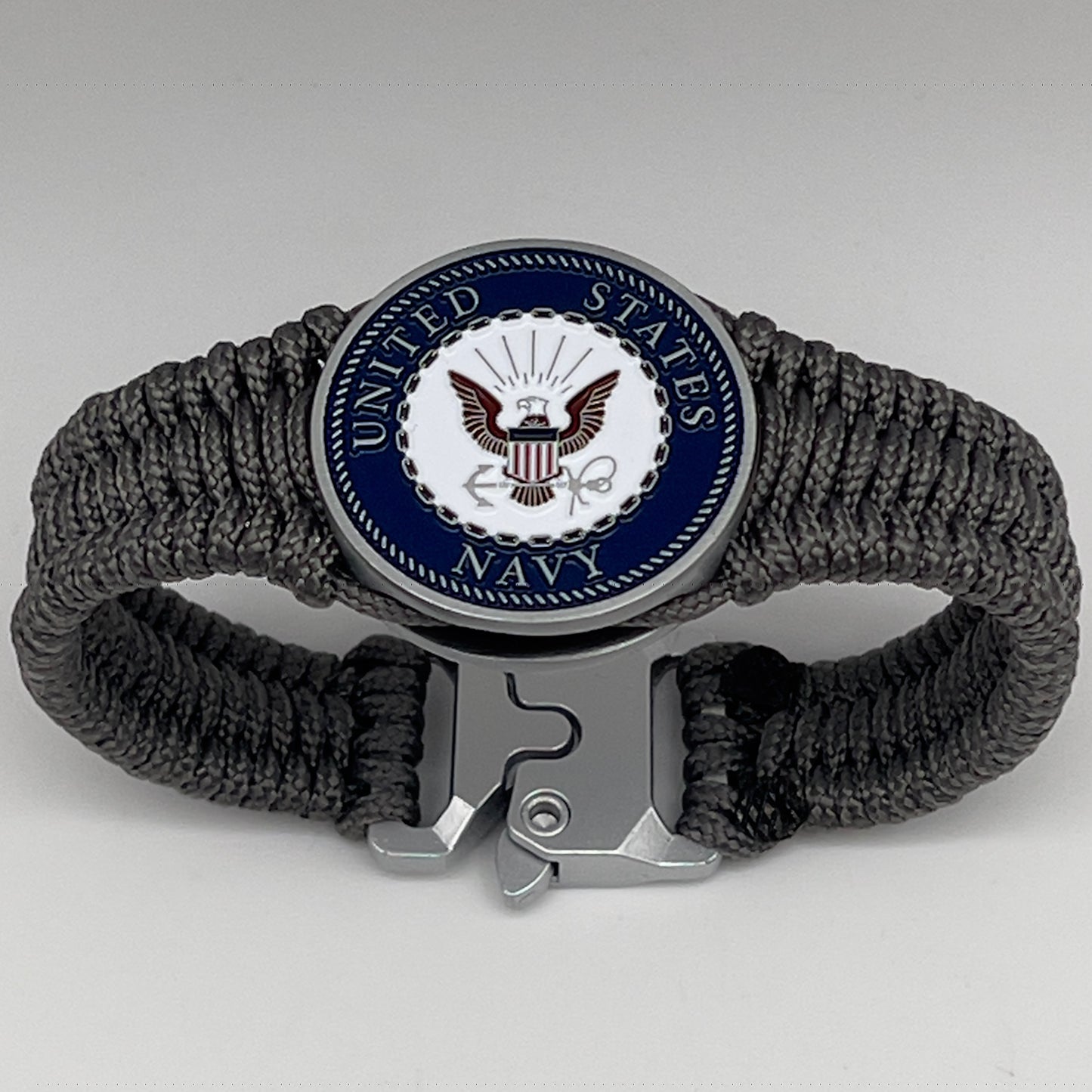 Thin, narrow, flexible and comfortable braided United States Navy bracelet featuring an antique silver plated Navy medallion, a silver Cobra style tactical buckle and woven with Charcoal Gray Type-1 paracord.