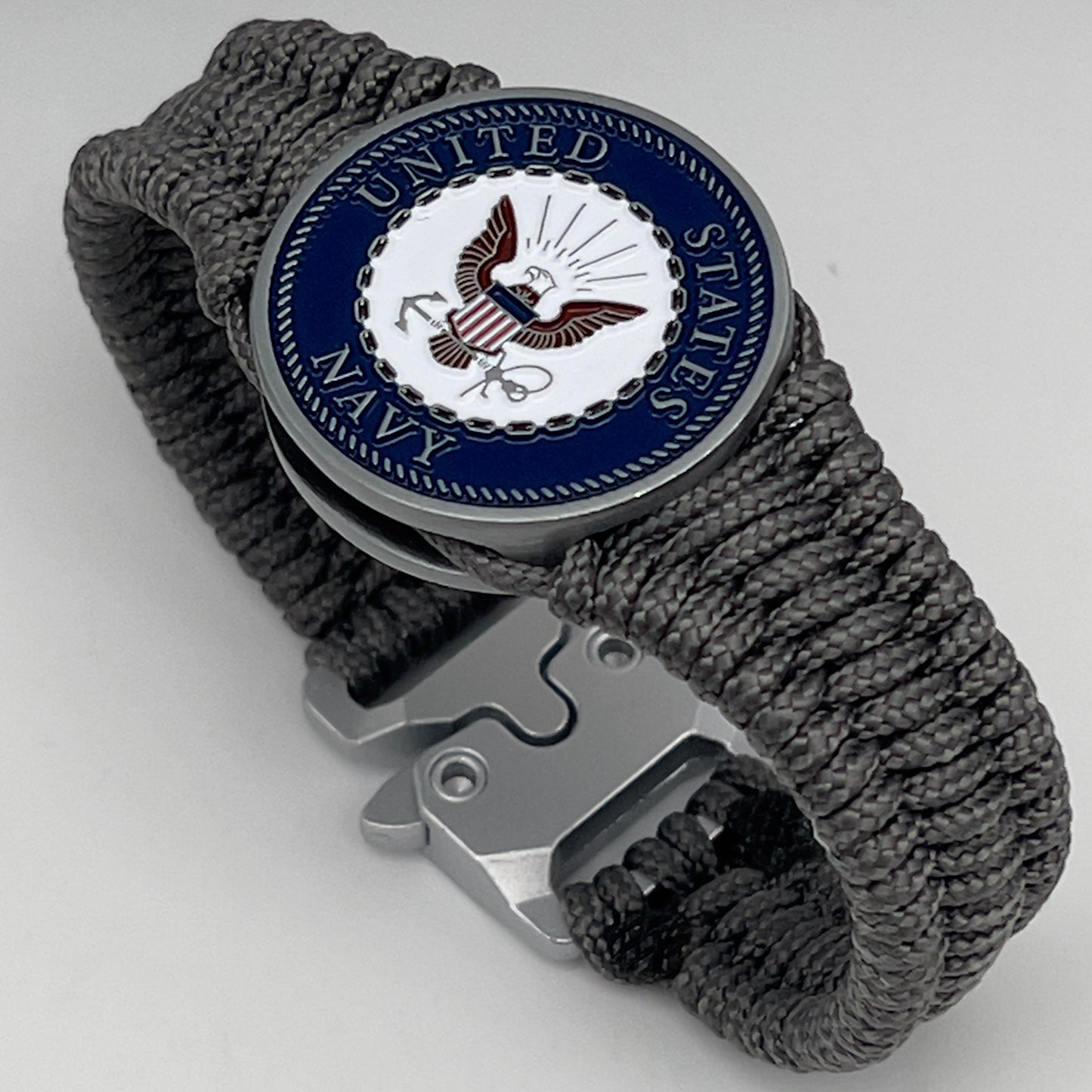 Thin, narrow, flexible and comfortable braided United States Navy bracelet featuring an antique silver plated Navy medallion, a silver Cobra style tactical buckle and woven with Charcoal Gray Type-1 paracord.