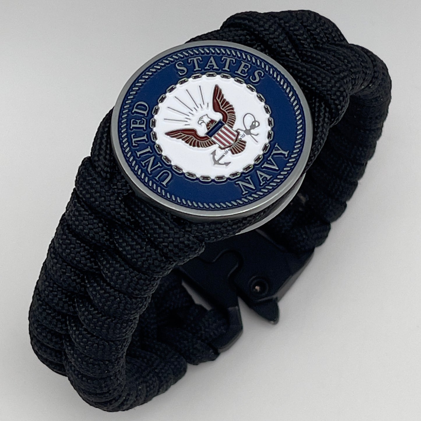 Thick, narrow, and semi-rigid braided United States Navy bracelet featuring an antique silver plated Navy medallion, a black Cobra style tactical buckle and woven with black 550 paracord.