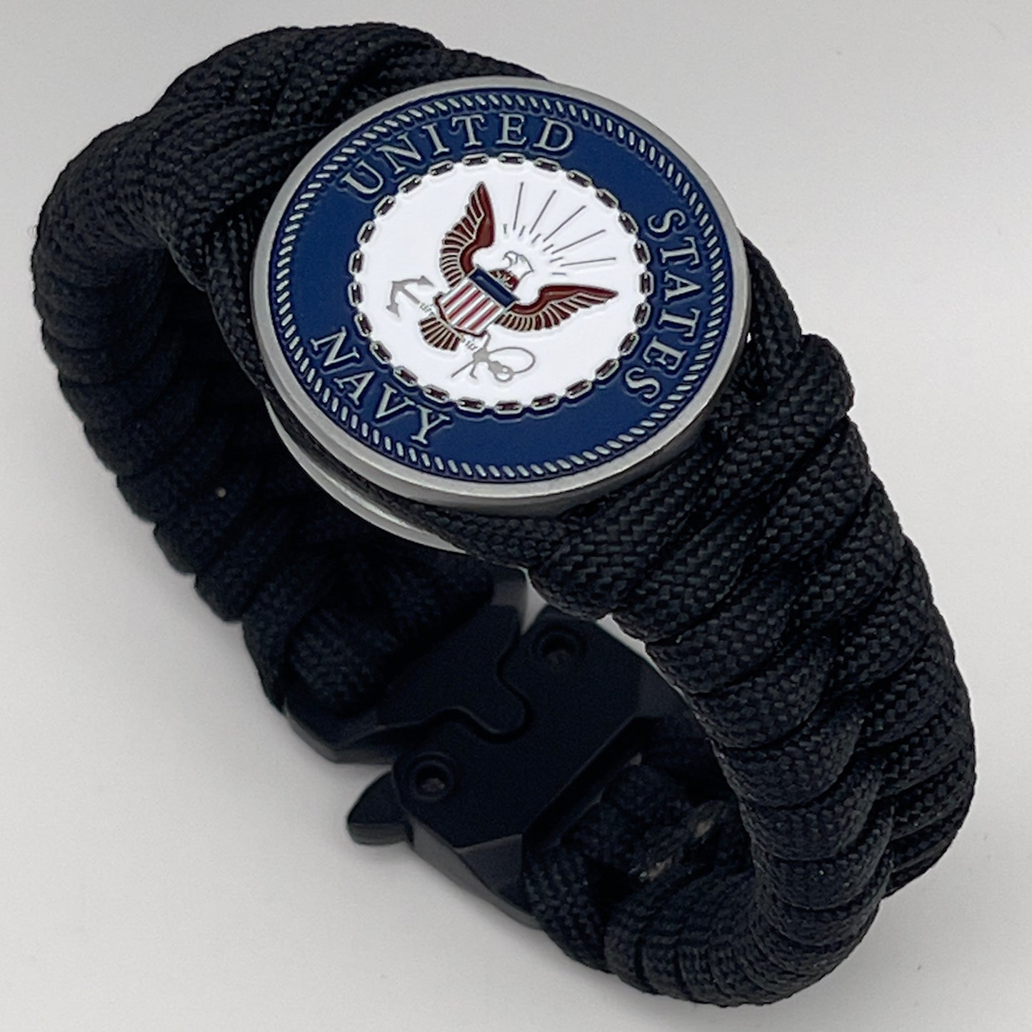 Thick, narrow, and semi-rigid braided United States Navy bracelet featuring an antique silver plated Navy medallion, a black Cobra style tactical buckle and woven with black 550 paracord.
