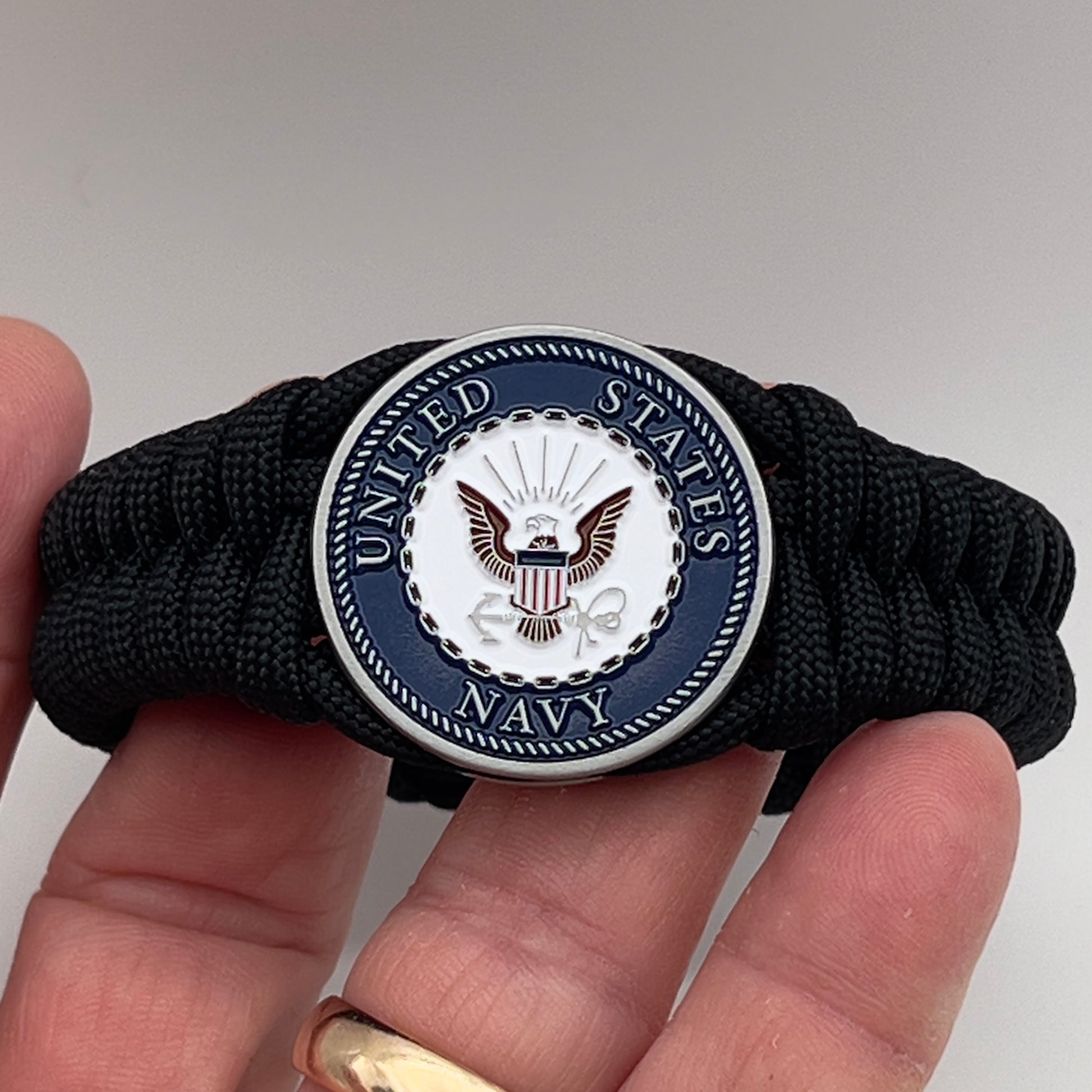 Thick, narrow, and semi-rigid braided United States Navy bracelet featuring an antique silver plated Navy medallion, a black Cobra style tactical buckle and woven with black 550 paracord.