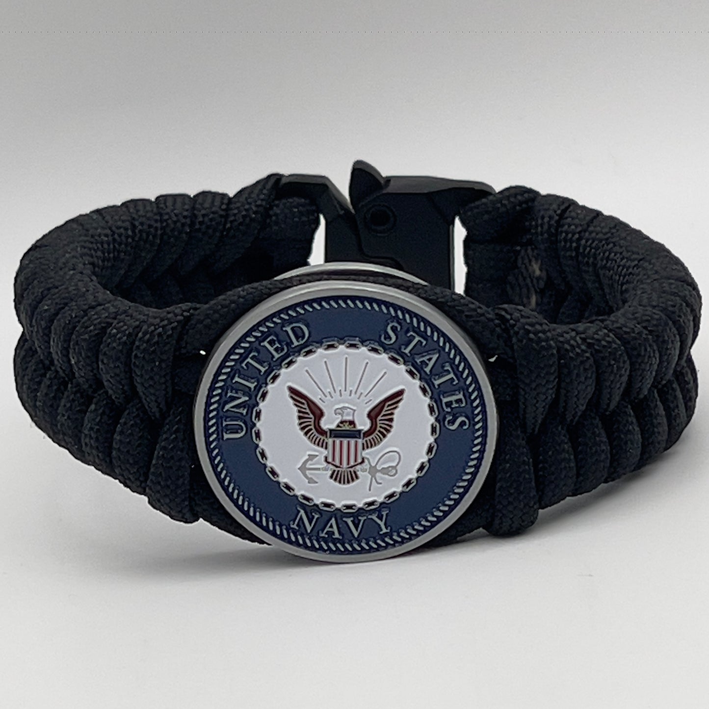 Thick, narrow, and semi-rigid braided United States Navy bracelet featuring an antique silver plated Navy medallion, a black Cobra style tactical buckle and woven with black 550 paracord.