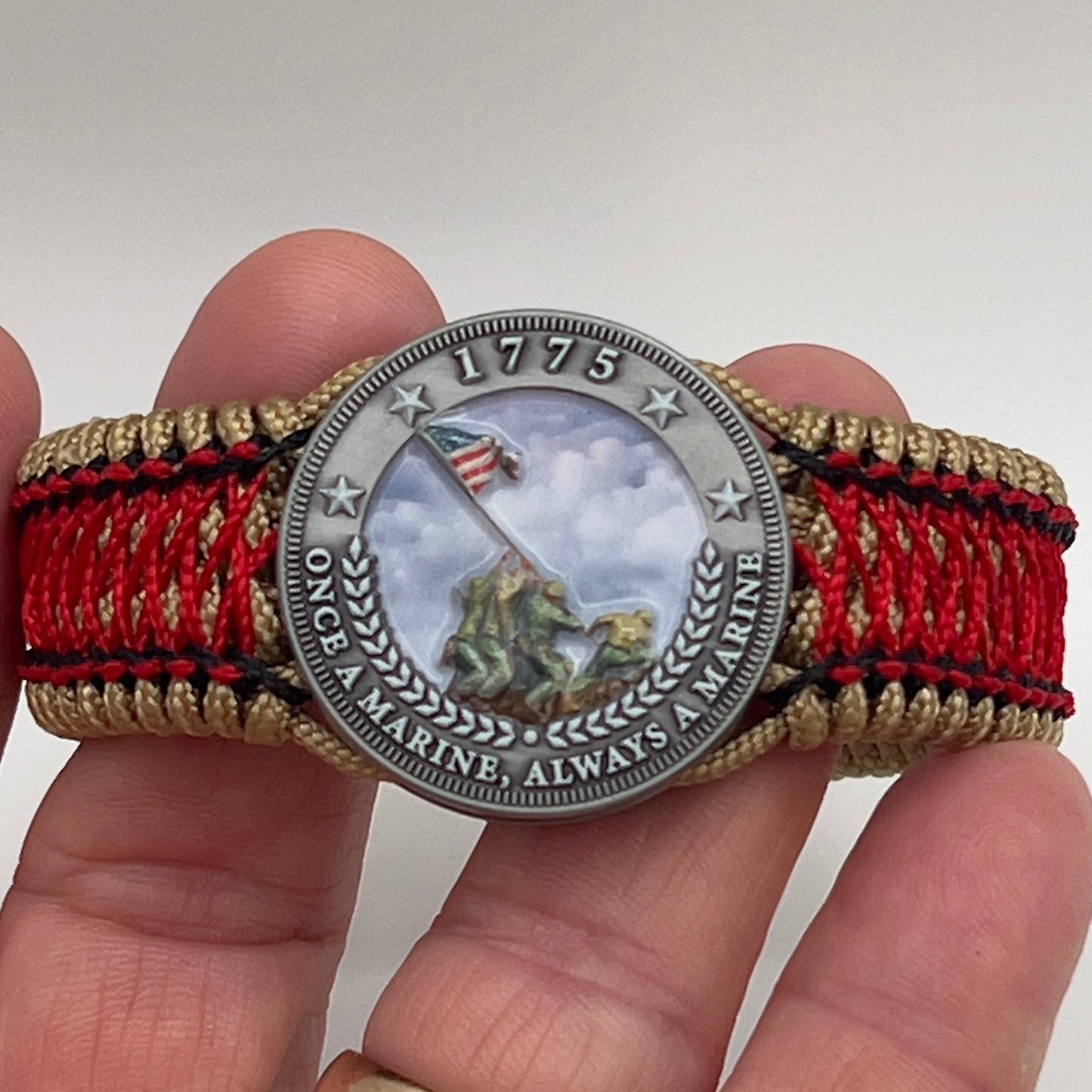 Thin, medium width, flexible and comfortable braided United States Marine Corps Iwo Jima bracelet featuring a UV painted antique silver plated Iwo Jima flag raising medallion, a gold Cobra style tactical buckle and woven with gold Type-1 paracord and Imperial Red and black nano cord.