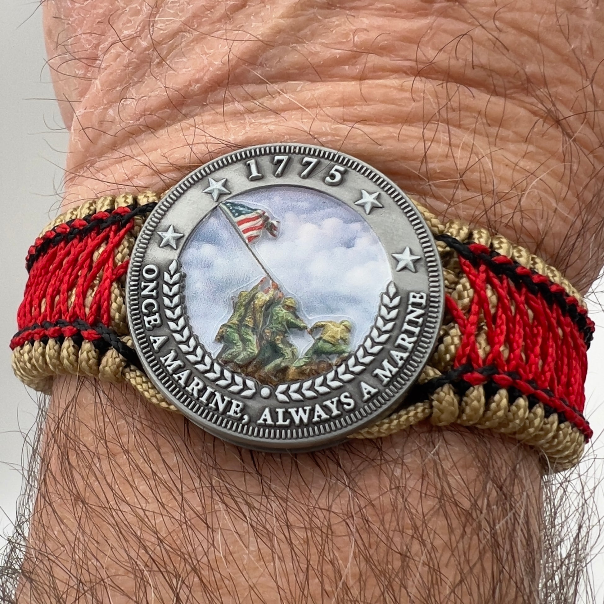 Thin, medium width, flexible and comfortable braided United States Marine Corps Iwo Jima bracelet featuring a UV painted antique silver plated Iwo Jima flag raising medallion, a gold Cobra style tactical buckle and woven with gold Type-1 paracord and Imperial Red and black nano cord.