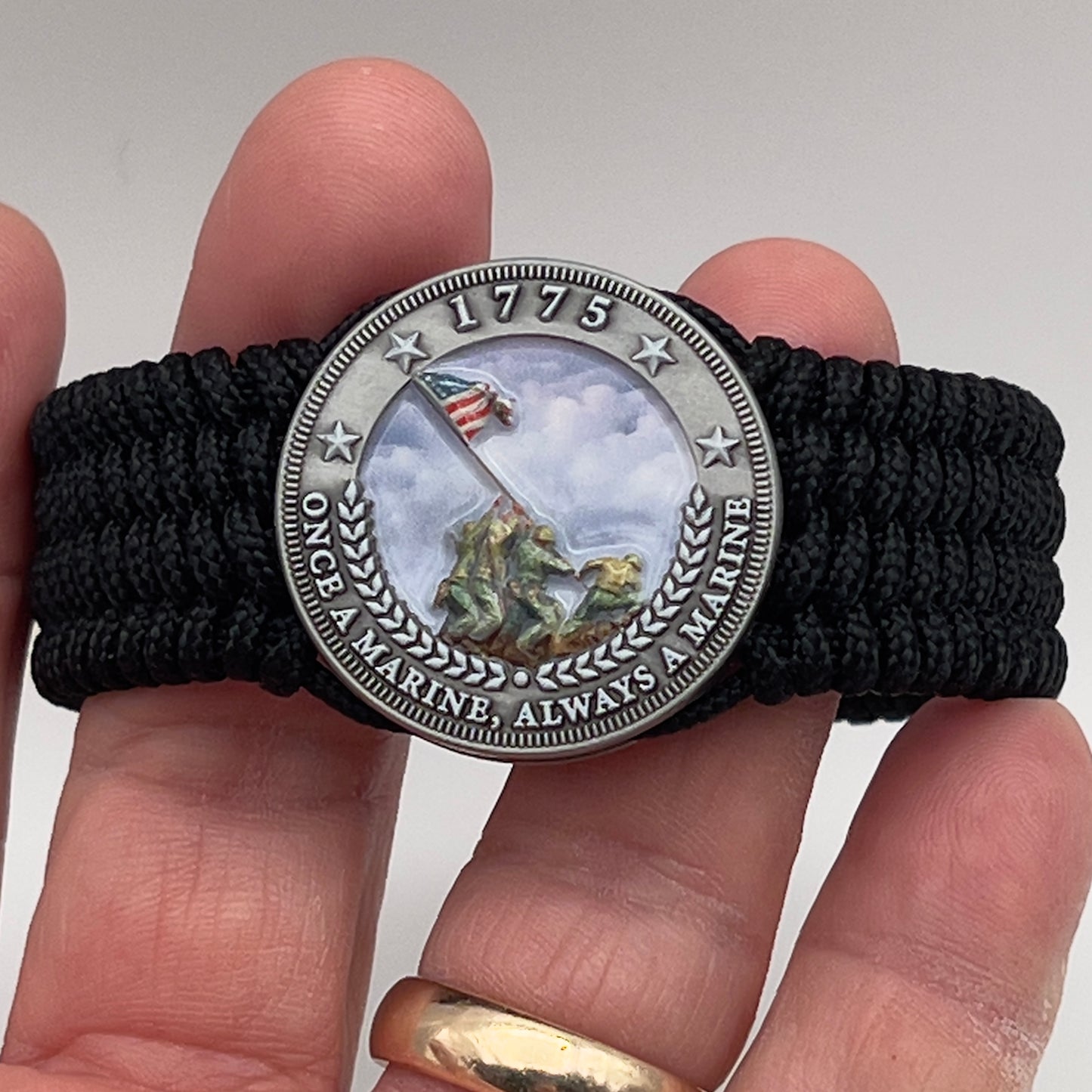 Thin, wide, flexible and comfortable braided United States Marine Corps Iwo Jima bracelet featuring an antique silver plated UV painted Iwo Jima flag raising medallion, a black Cobra style tactical buckle and woven with black Type-1 paracord.